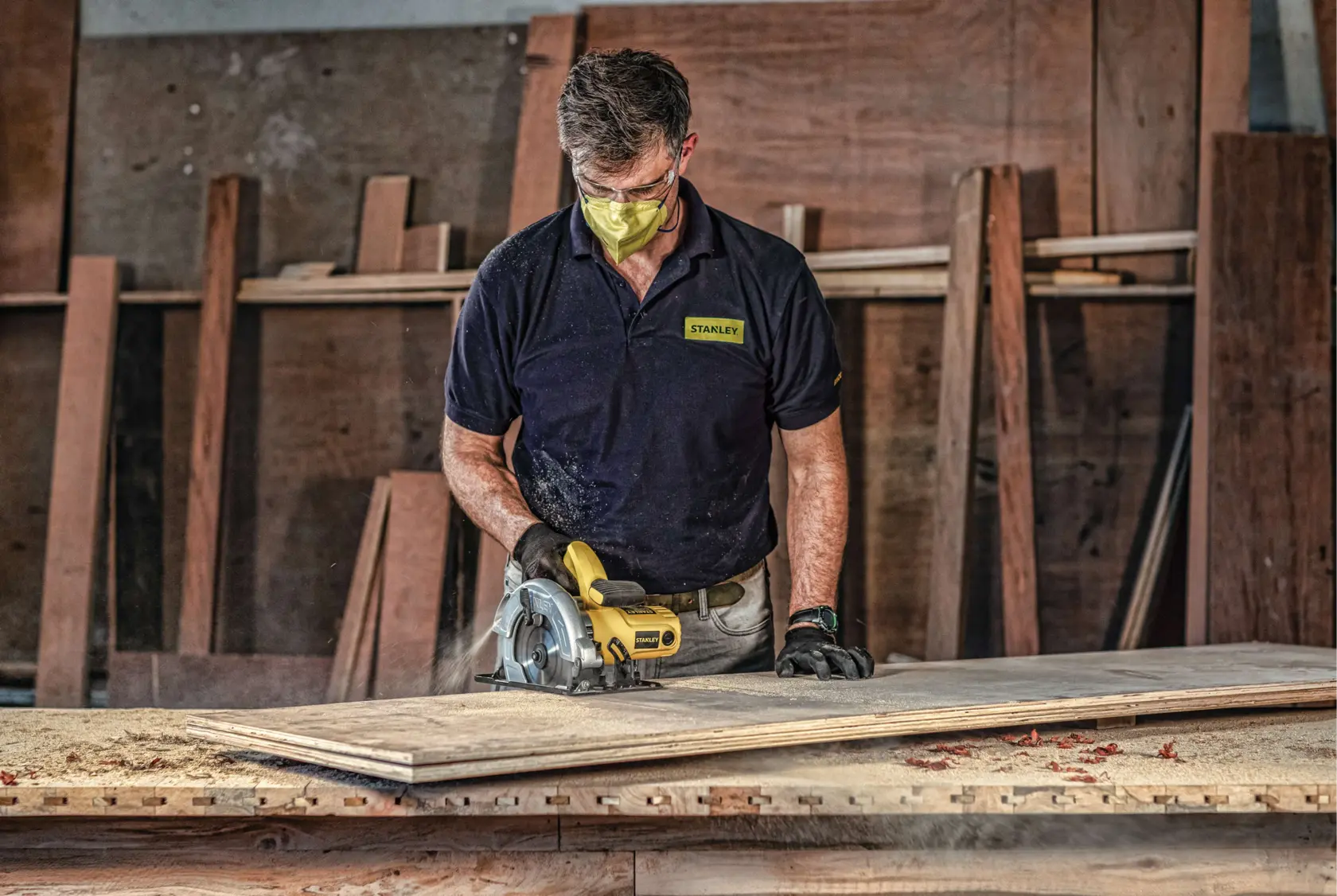 Sierra circular Stanley SC16 en uso sobre madera en taller, operario con camisa Stanley.