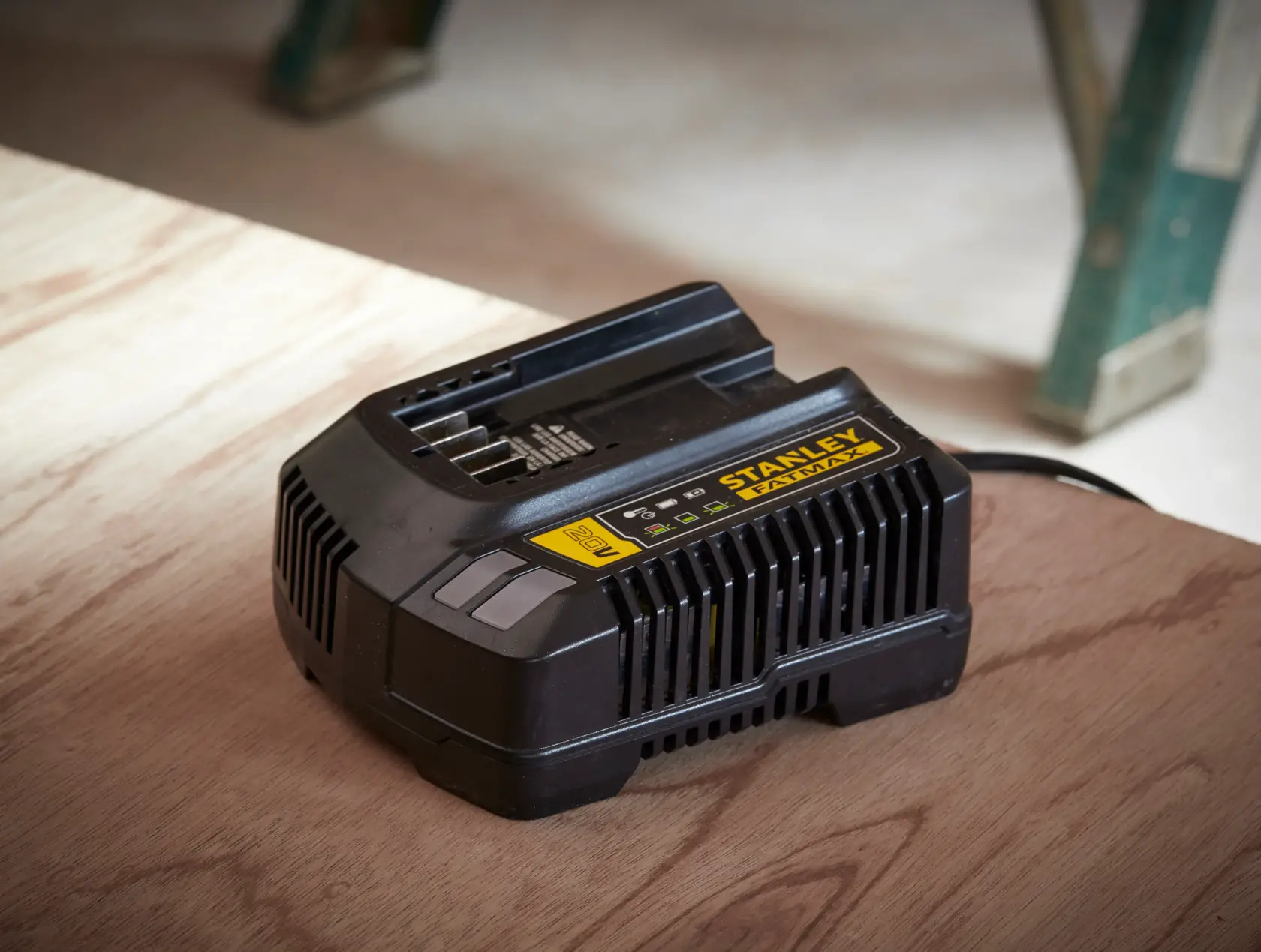 Cargador de batería Stanley SC200 negro con etiqueta amarilla, en ángulo sobre superficie de madera.