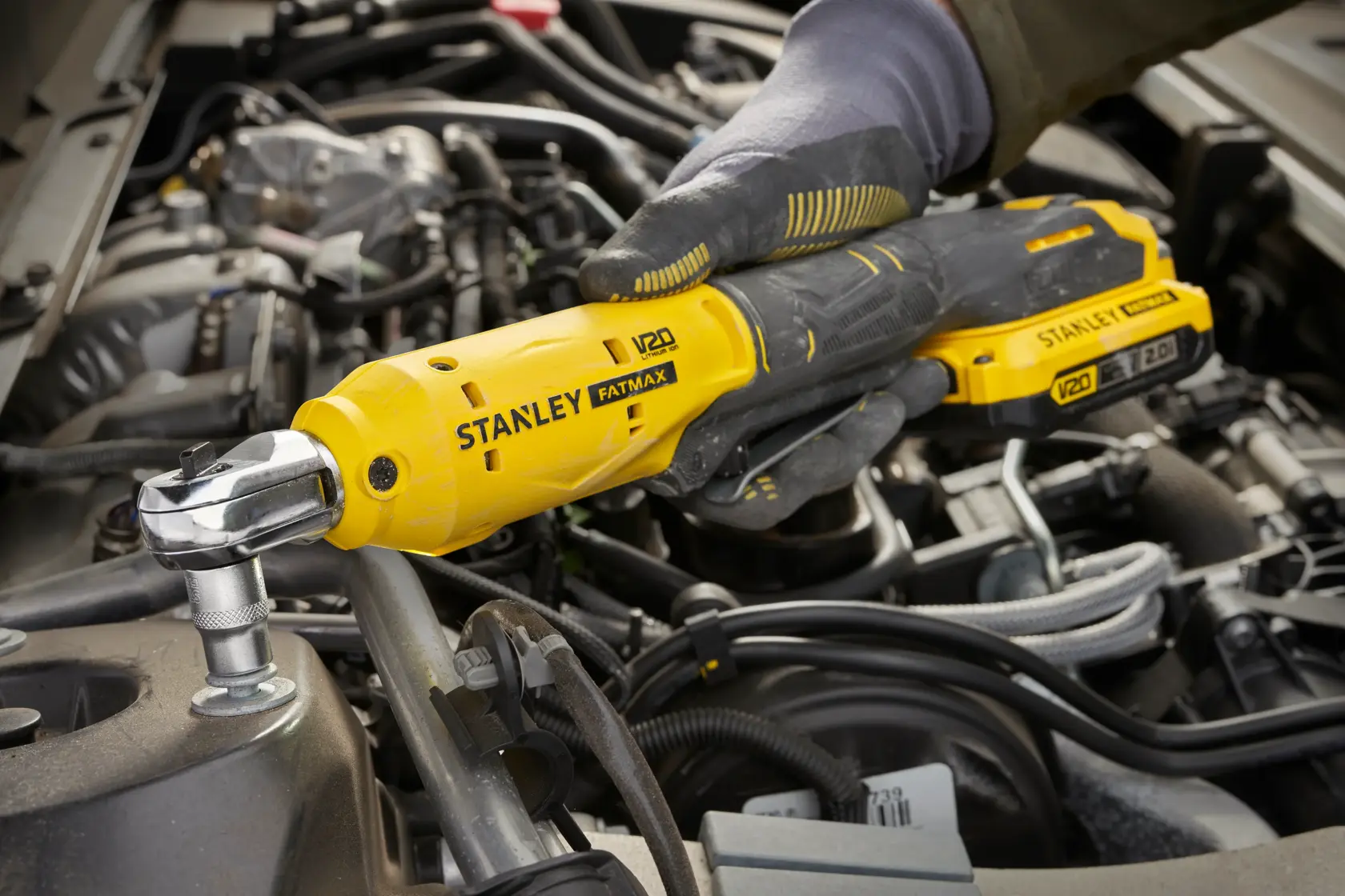 STANLEY SCF930 trinquete inalámbrico utilizado en un motor de coche, vista lateral cercana, herramienta amarilla y negra.