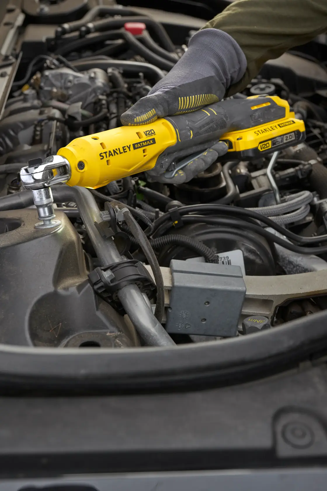 Fotografía de la carraca STANLEY SCF930 usada en un motor de automóvil, mano enguantada sosteniendo herramienta inalámbrica amarilla.
