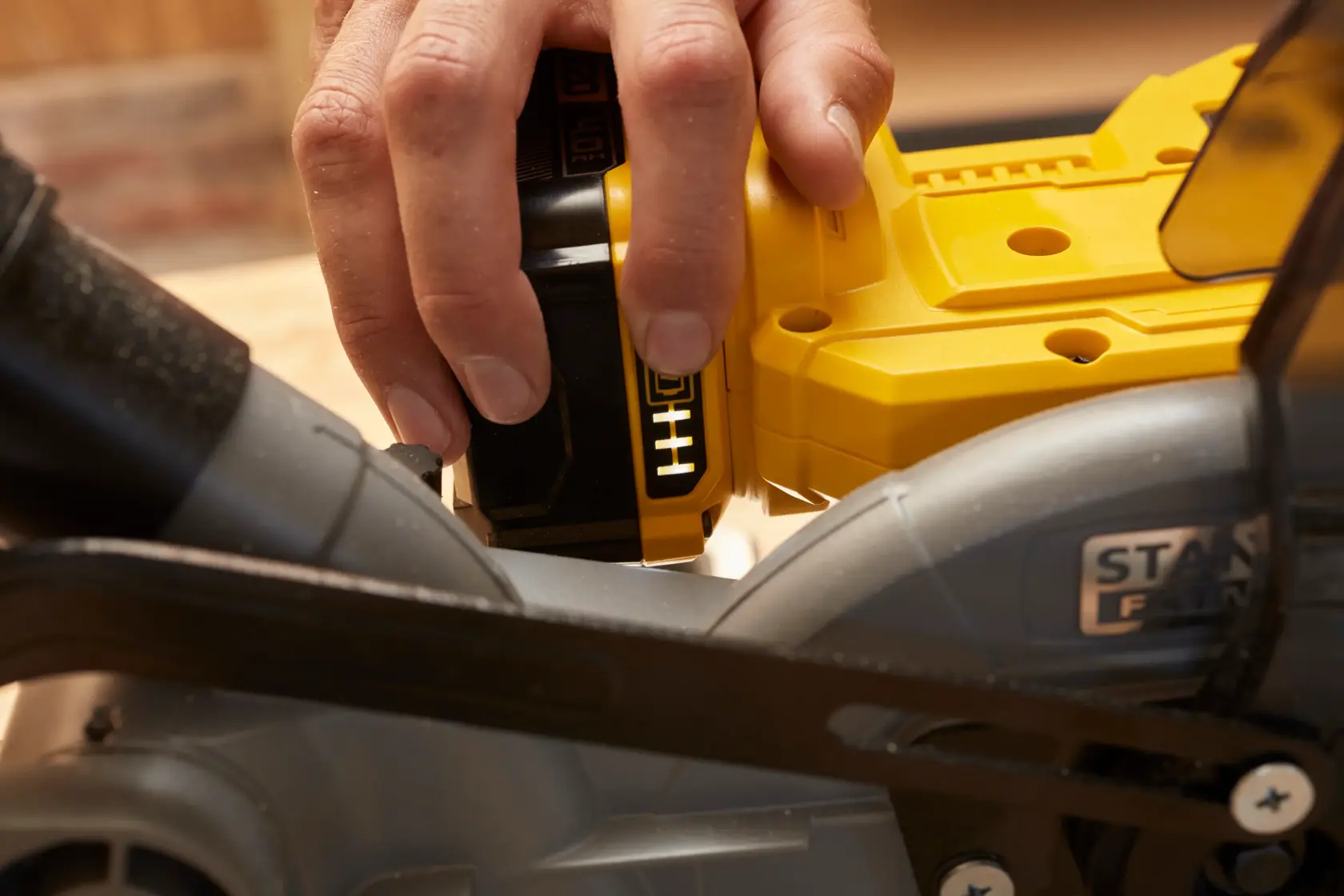 STANLEY SCM701-B3 sierra a batería, primer plano del cuerpo amarillo y mano insertando la batería.