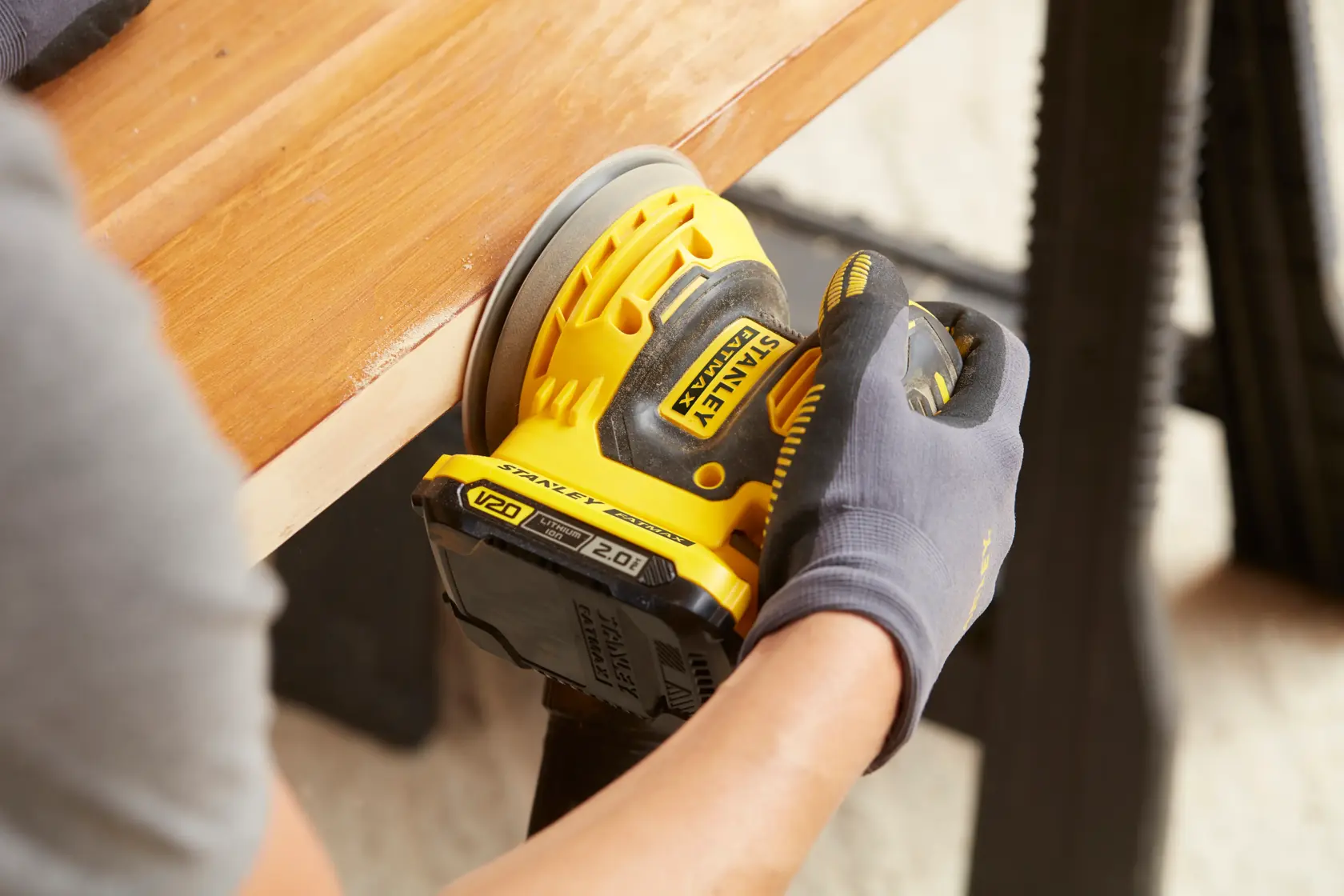 Fotografía de la lijadora inalámbrica STANLEY SCS220D1S-B2 en uso sobre madera, diseño amarillo y negro, mano con guante.