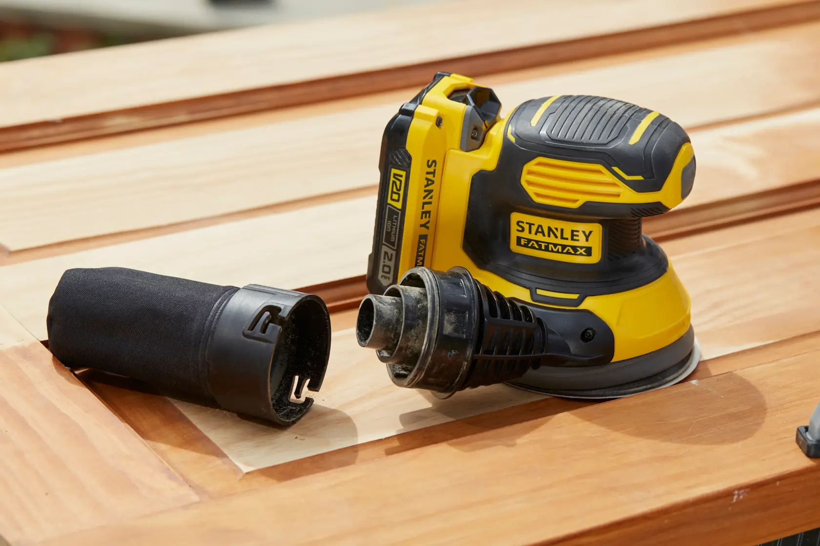 Lijadora inalámbrica STANLEY SCS220D1S-B2 con accesorio para recolección de polvo, amarilla y negra, sobre superficie de madera.
