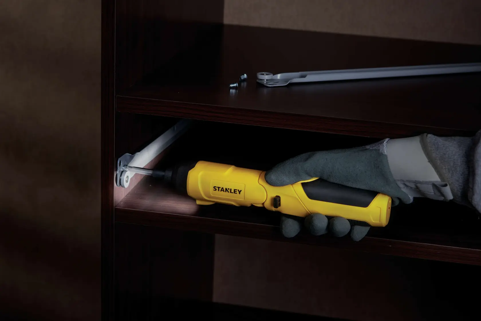 Fotografía del destornillador inalámbrico amarillo STANLEY SCS4K en uso ensamblando un mueble de madera oscura, vista lateral.