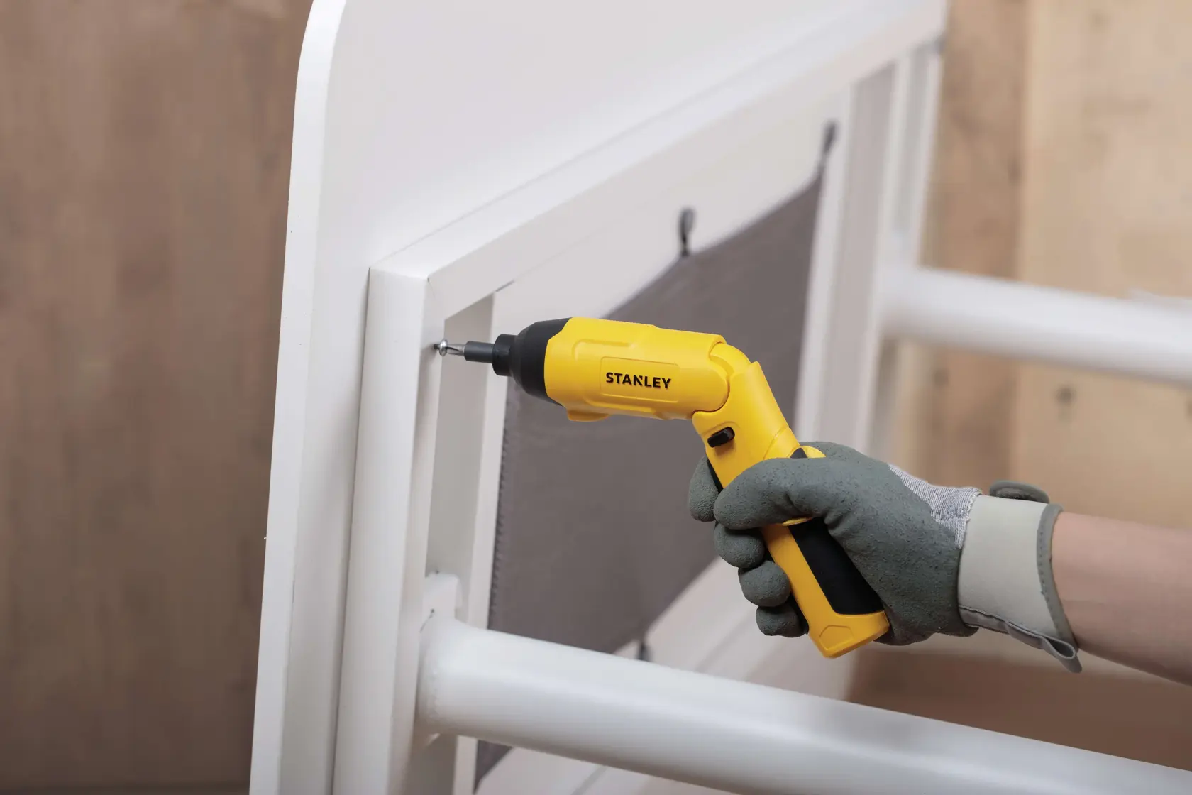 Destornillador inalámbrico STANLEY SCS4K en uso ensamblando mueble blanco, ángulo lateral.