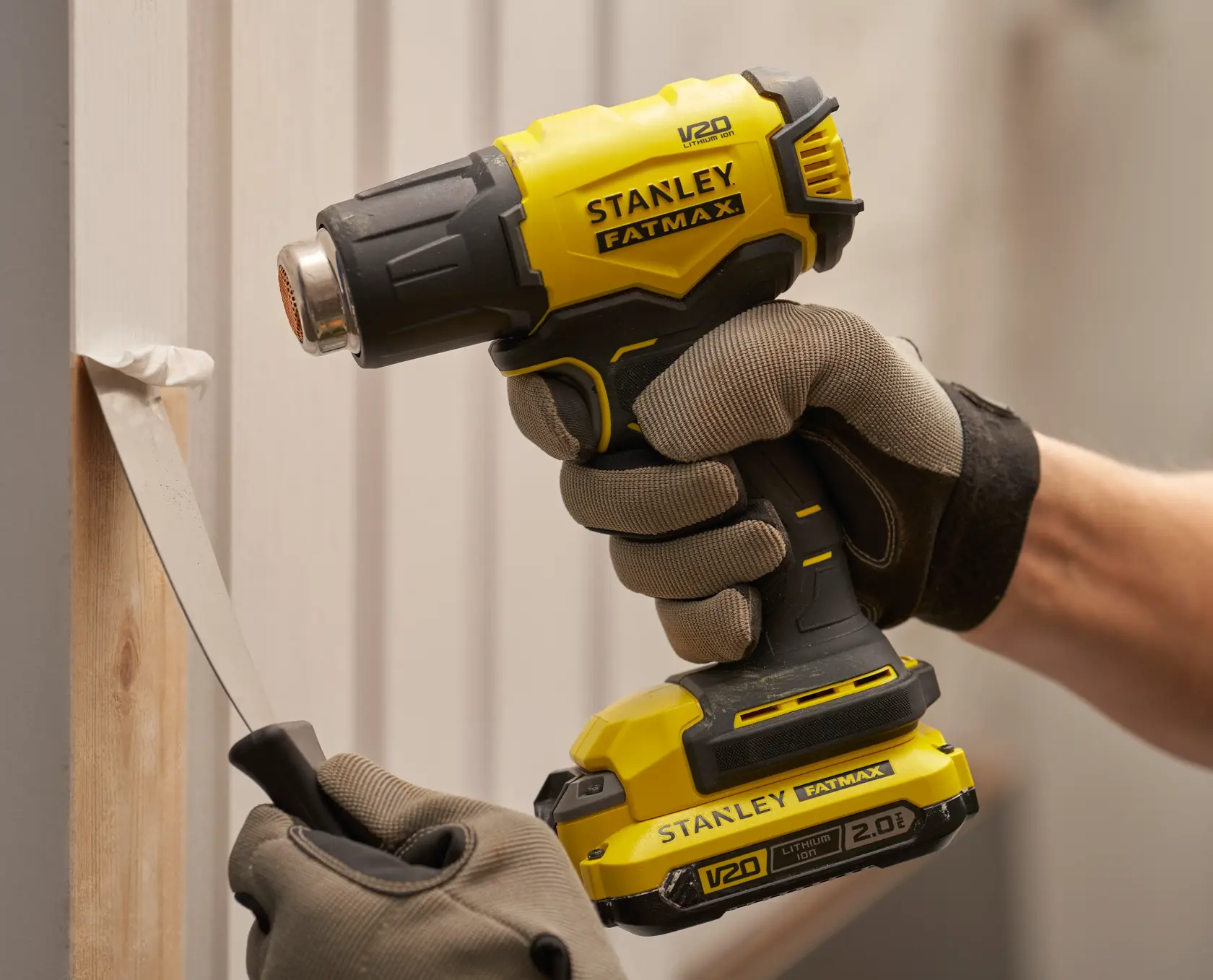 Pistola de calor inalámbrica Stanley SCX530B-B3 utilizada para quitar pintura, herramienta en manos enguantadas en primer plano.
