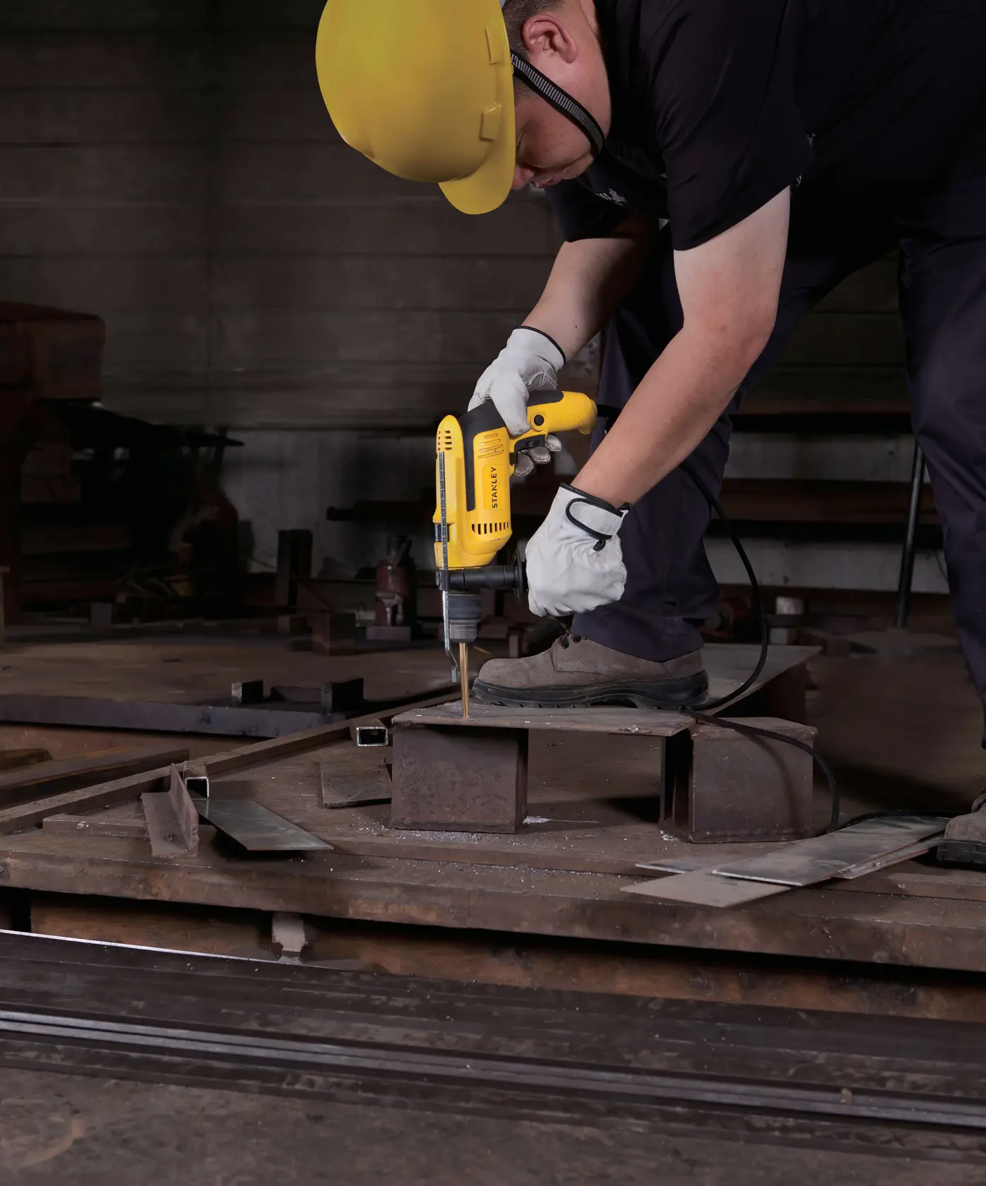 Taladro con cable STANLEY SDH700K usado por trabajador con guantes y casco perforando placa metálica en taller.