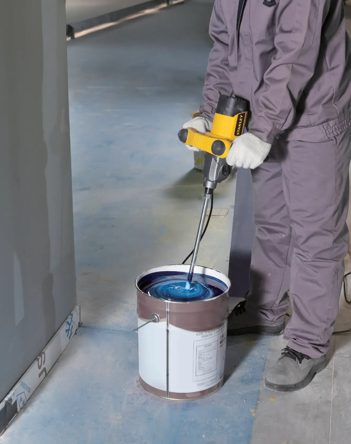Mezclador eléctrico STANLEY SDR1400-KR en uso, mezclando pintura azul en un cubo grande sobre un suelo de obra.