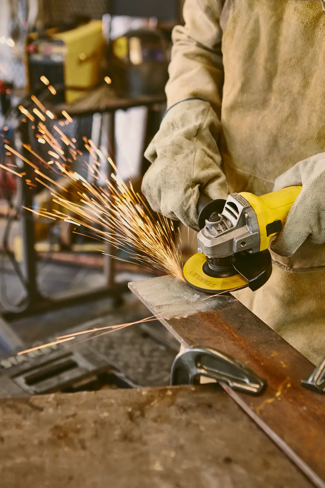Fotografía de la amoladora angular STANLEY SG6115-B2C en uso con cuerpo amarillo, genera chispas al pulir metal.
