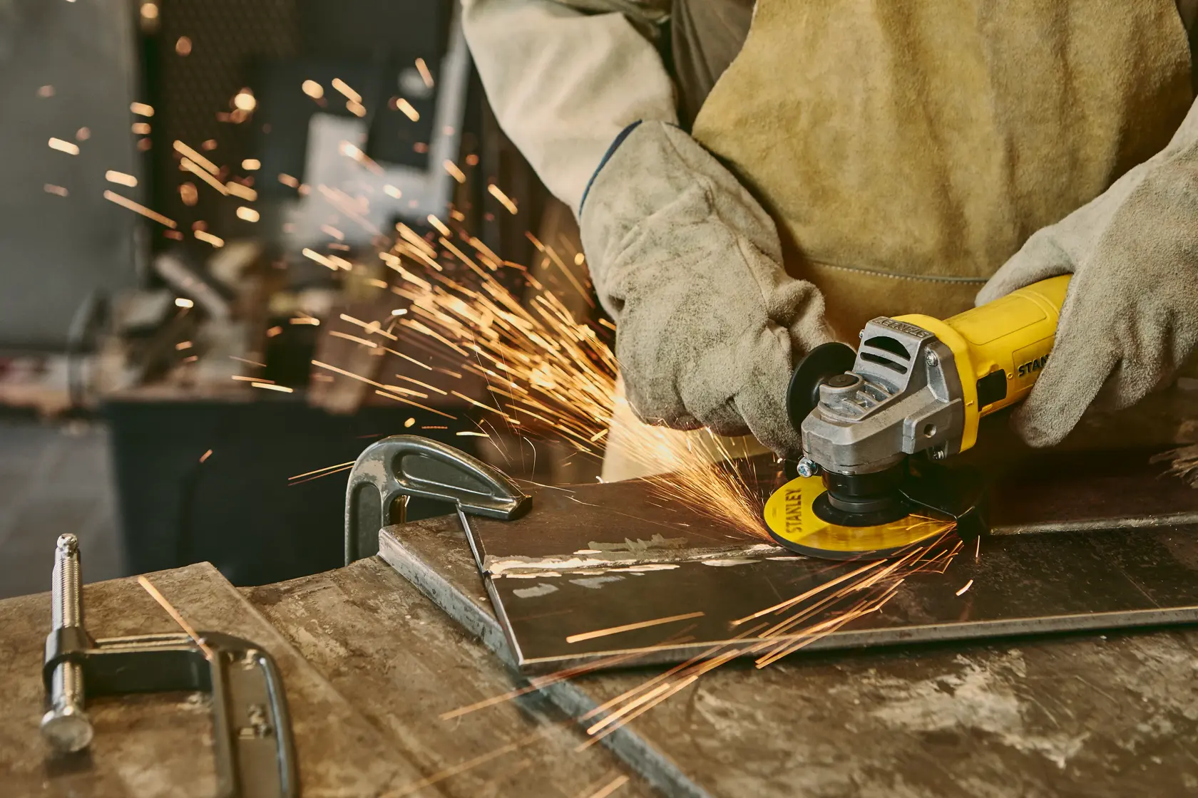 Amoladora angular STANLEY SG6115-B2C en uso, cortando metal con chispas, primer plano en taller.