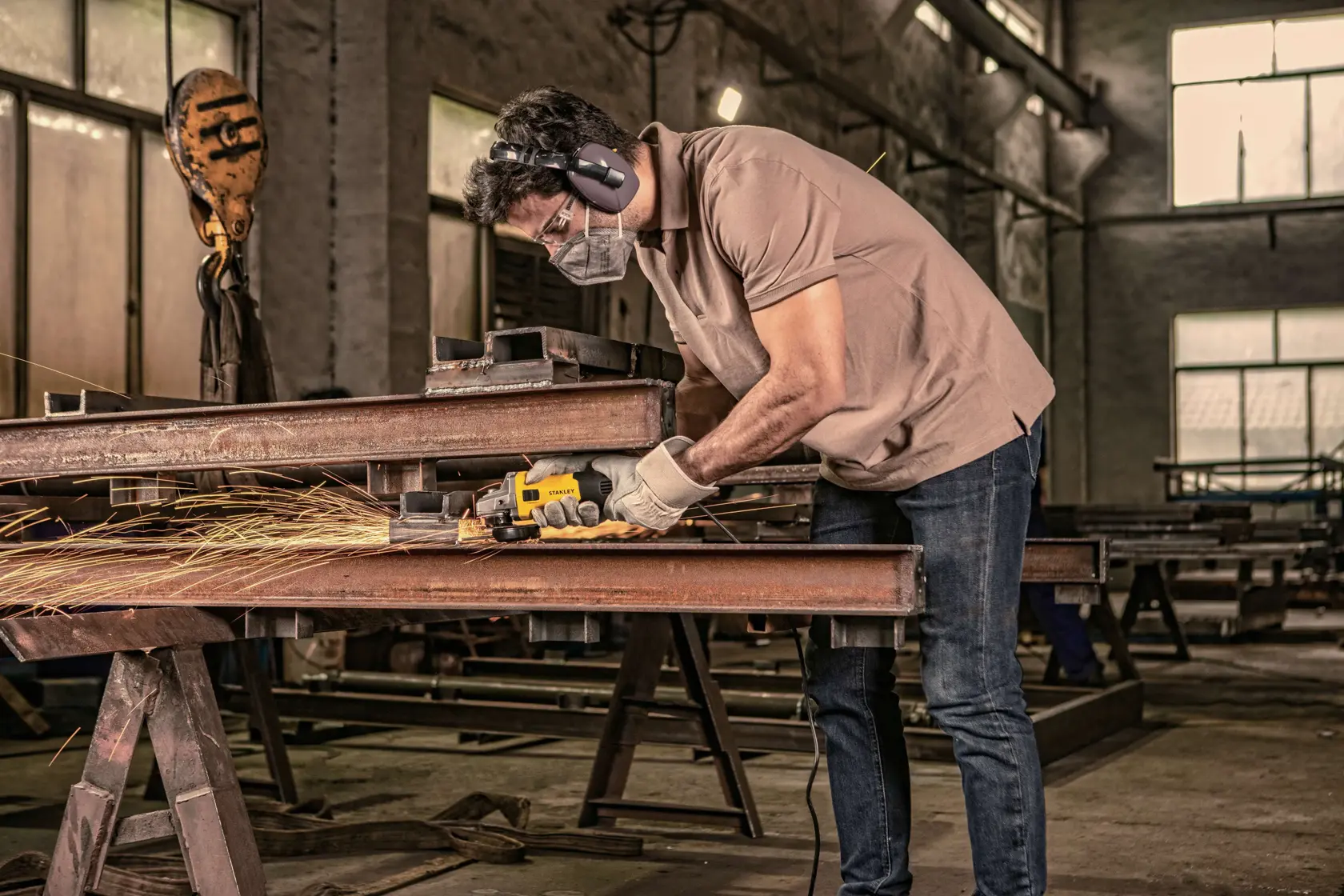 STANLEY SG7115-B3 amoladora angular utilizada por trabajador cortando vigas metálicas en taller industrial.