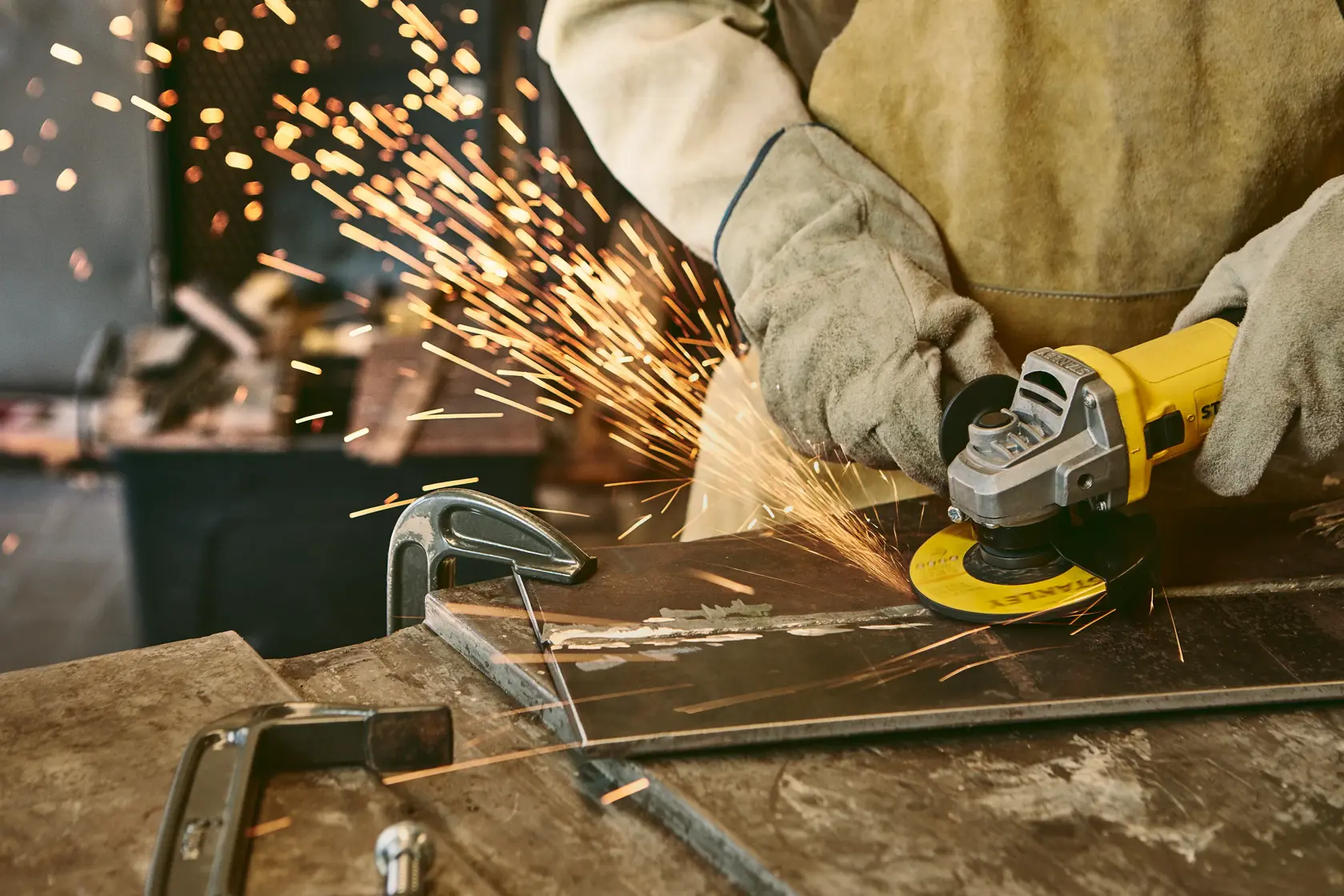 Stanley SG7115-B3 amoladora angular en uso cortando metal, chispas, trabajador con guantes y equipo protector.