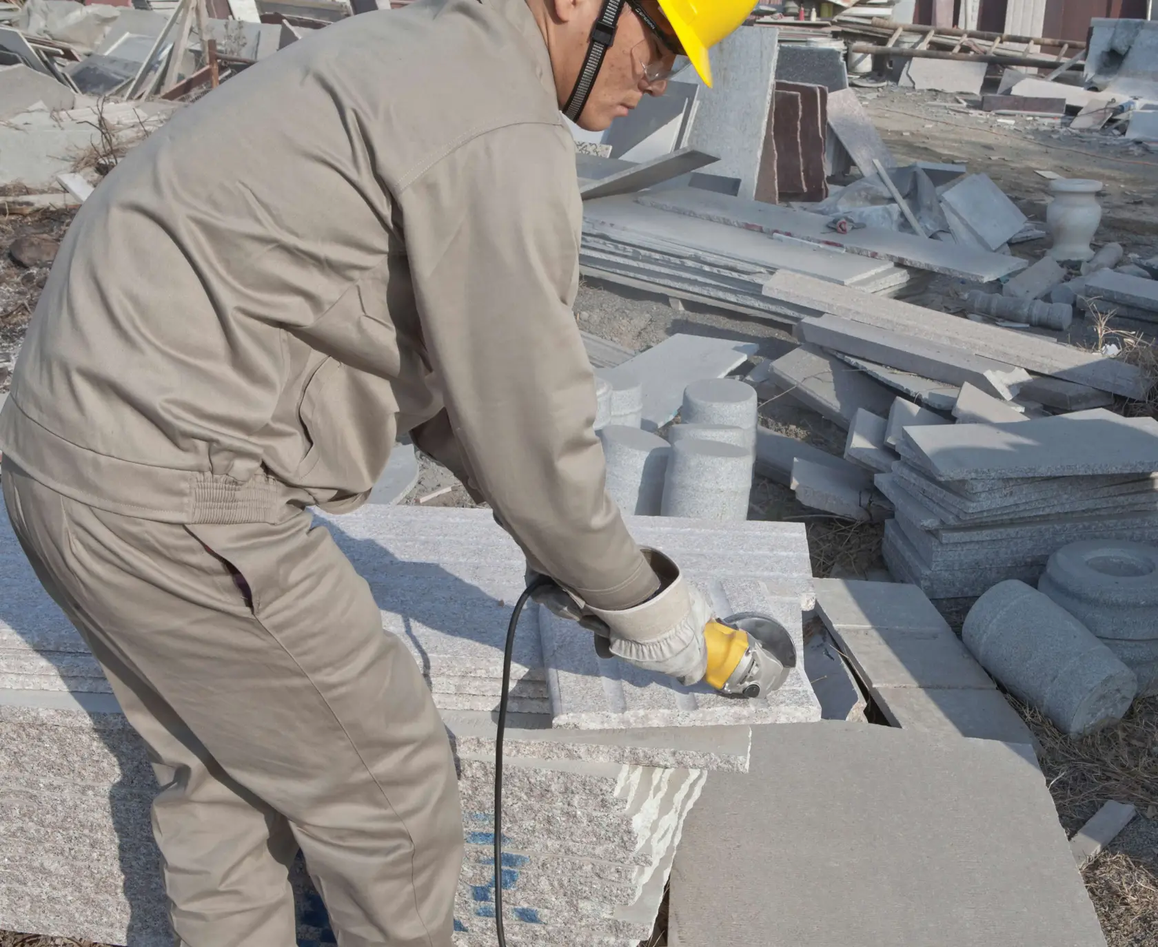 Amoladora angular STANLEY SGS1045K en uso, trabajador cortando losa de piedra al aire libre, vista lateral cercana.