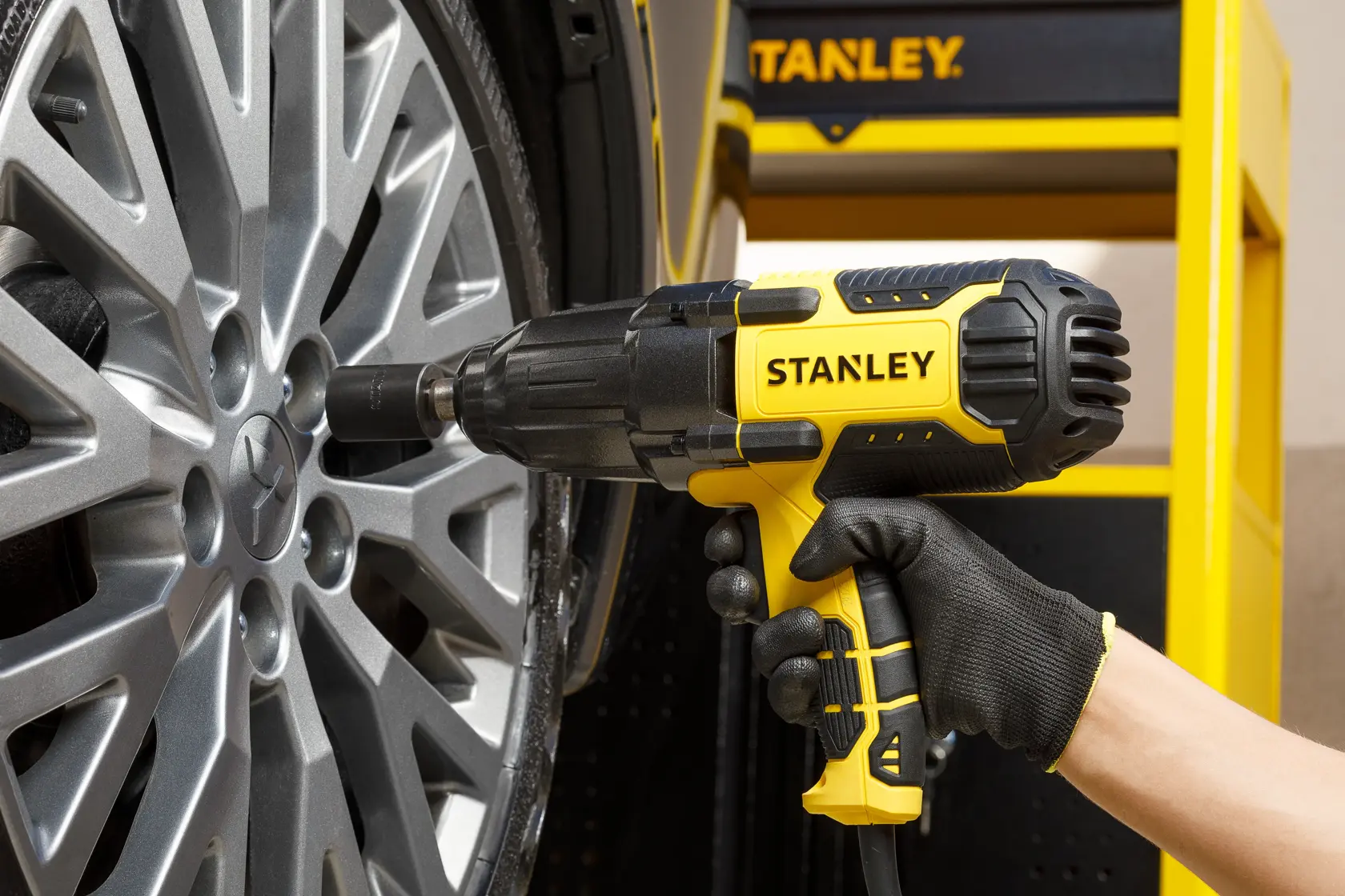 LLave de impacto STANLEY SIW901-B2 en uso apretando una rueda de auto, vista lateral en primer plano.