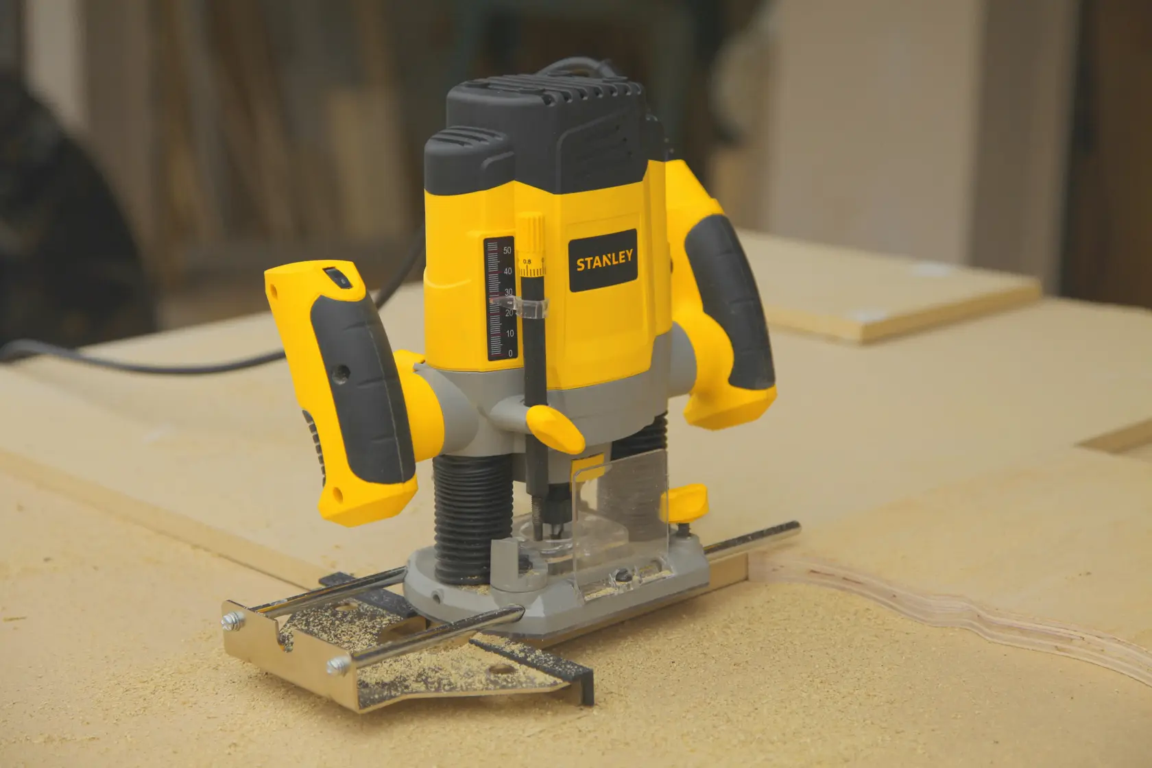 Foto del router de inmersión STANLEY SRR1200-AR con cuerpo amarillo y negro sobre superficie de madera en taller.