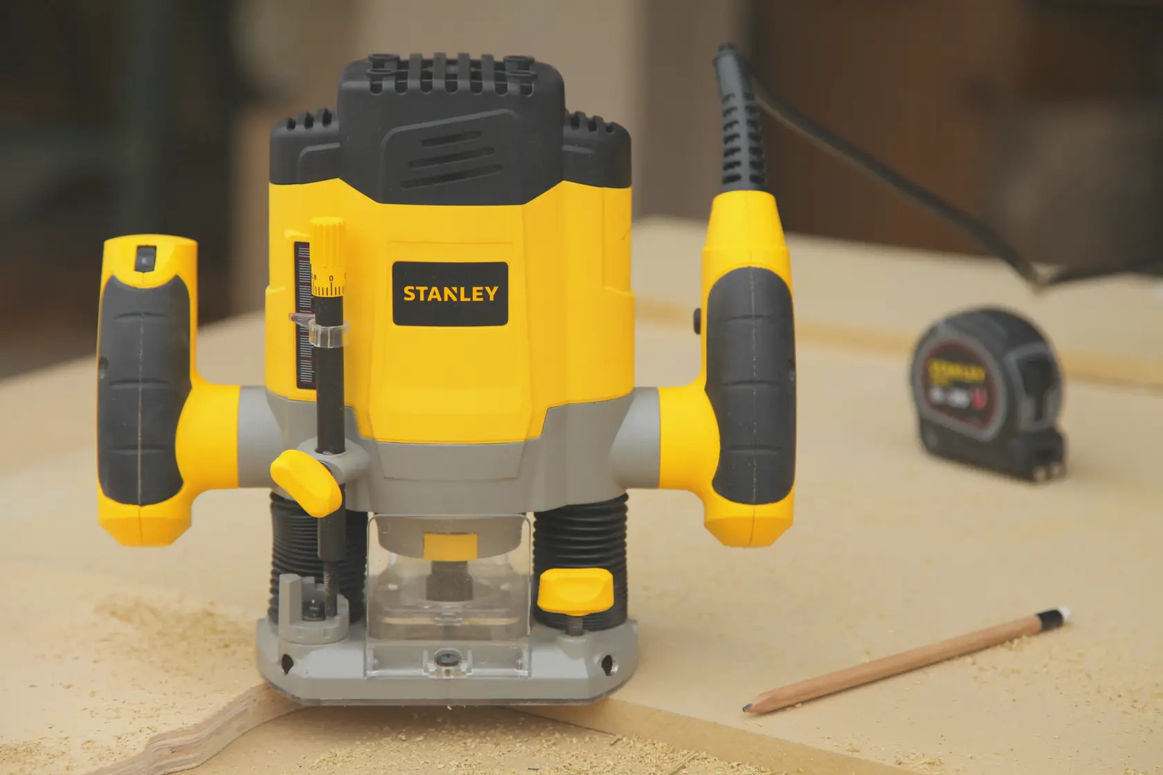 Stanley SRR1200-AR herramienta fresadora amarilla y negra, vista frontal, sobre banco con lápiz y cinta métrica.