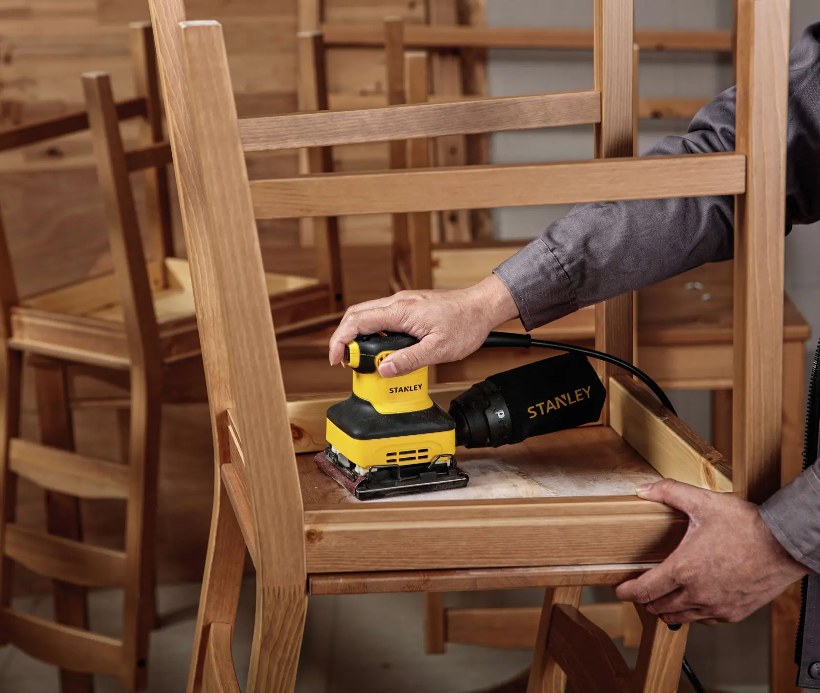 Fotografía de lijadora STANLEY SS24-B3 utilizada en una silla de madera, manual, contexto de carpintería.