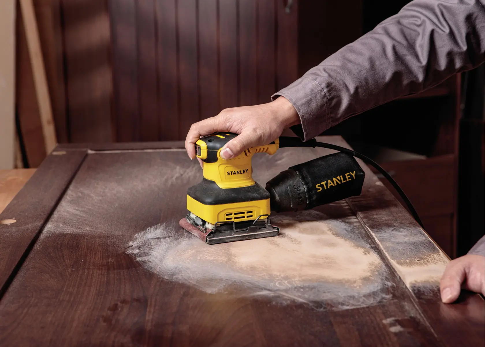 Lijadora de hojas STANLEY SS24-B3 usada para lijar una superficie de madera, vista cercana con colector de polvo visible.