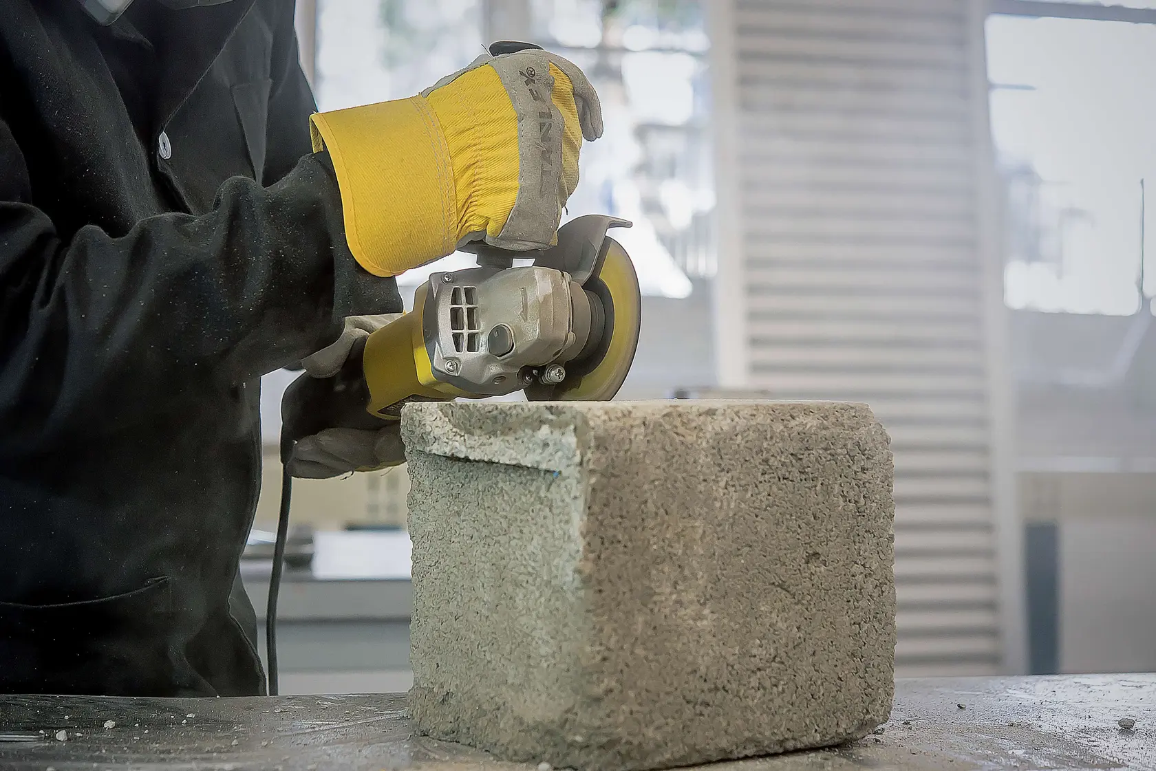 Amoladora angular STANLEY STA8070 en uso cortando un bloque de concreto, usuario con guantes de seguridad amarillos.