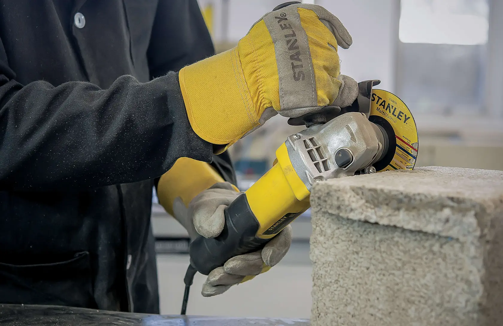 Fotografía Stanley STA8070 de amoladora angular amarilla cortando bloque de concreto, operador con guantes Stanley.