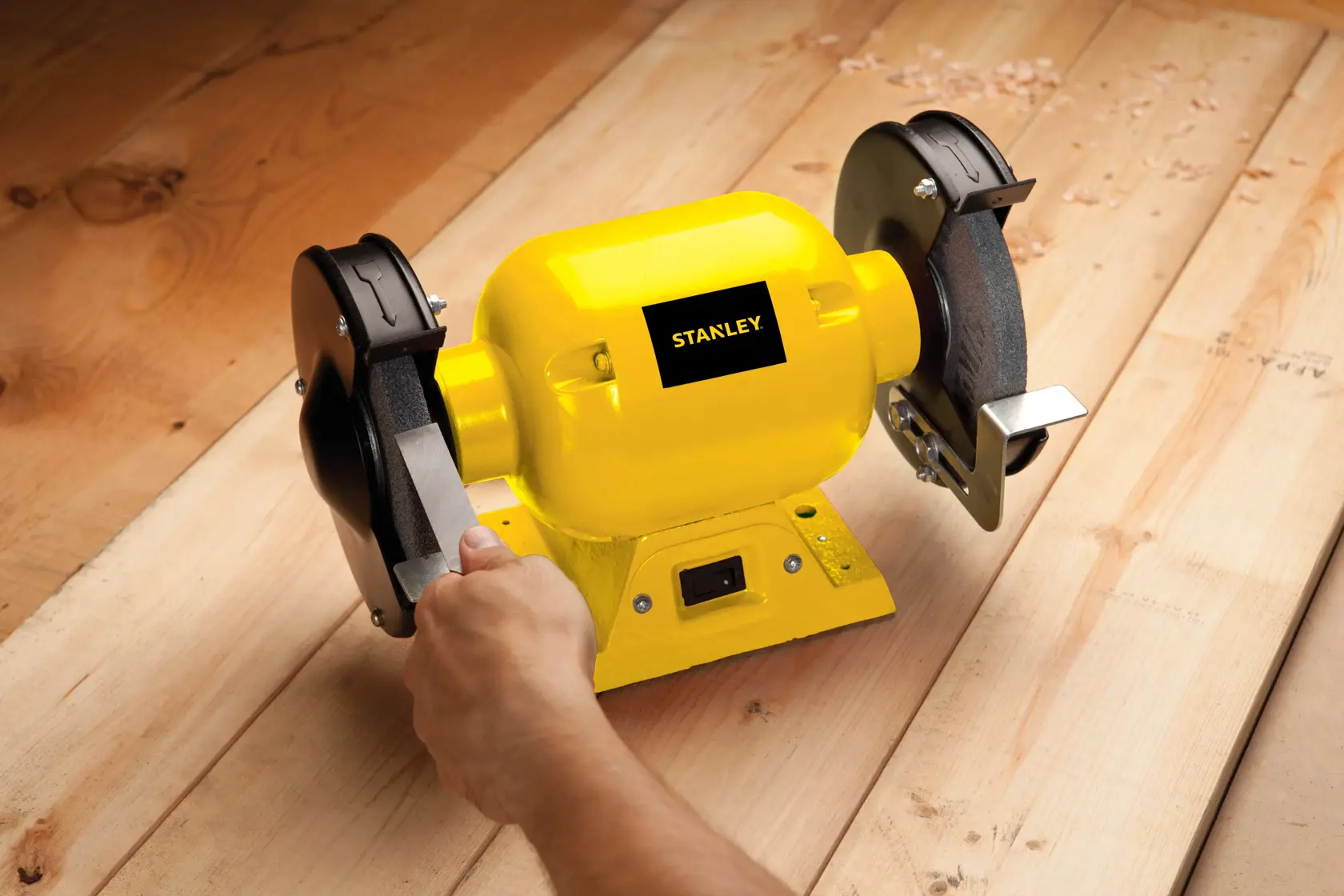 STANLEY STGB3715 esmeriladora de banco amarilla en uso sobre superficie de madera, vista lateral en primer plano.