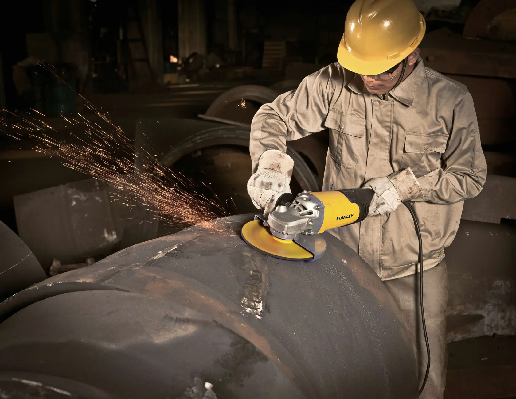 Fotografía de un trabajador usando la amoladora angular STANLEY STGL2223 en una gran tubería metálica, generando chispas.