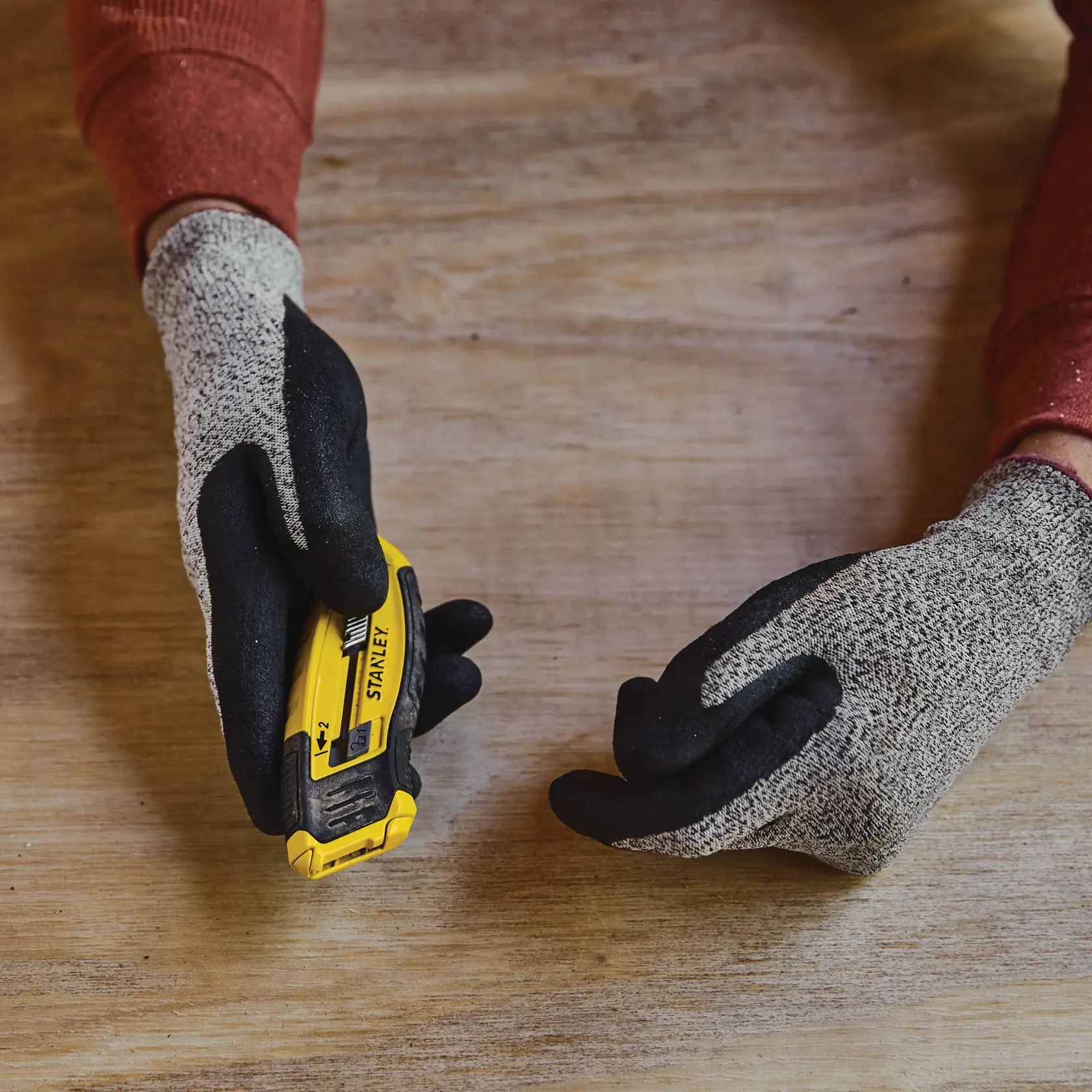 Fotografía del cuchillo utilitario STANLEY STHT10432 sostenido con guantes sobre una superficie de madera.
