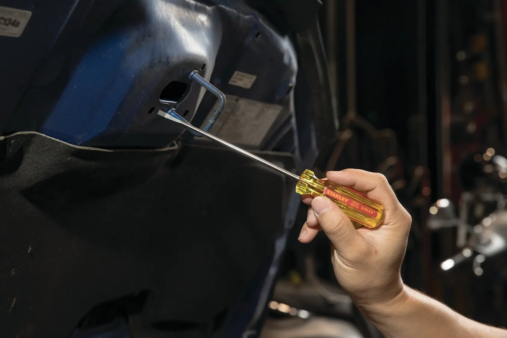 Destornillador STANLEY STHT69112 con mango amarillo usado en un tornillo interior de auto, vista lateral.