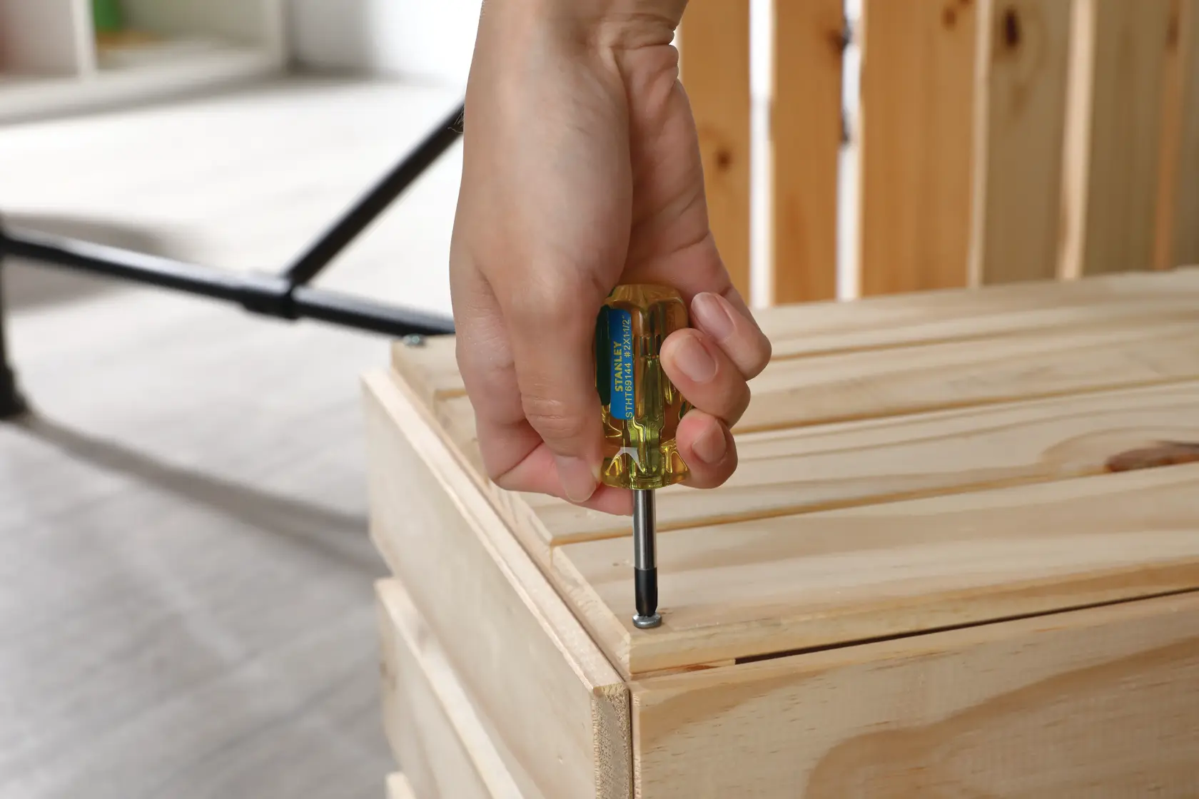 Fotografía de una mano usando un destornillador STANLEY STHT69144 para atornillar una caja de madera.