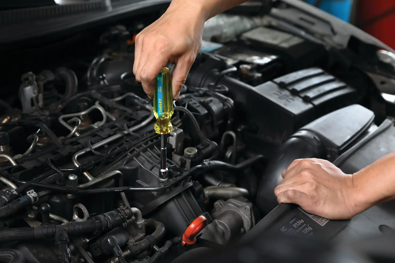 STANLEY STHT69185 destornillador en uso en un motor de automóvil, vista cercana, mango amarillo, reparación automotriz.