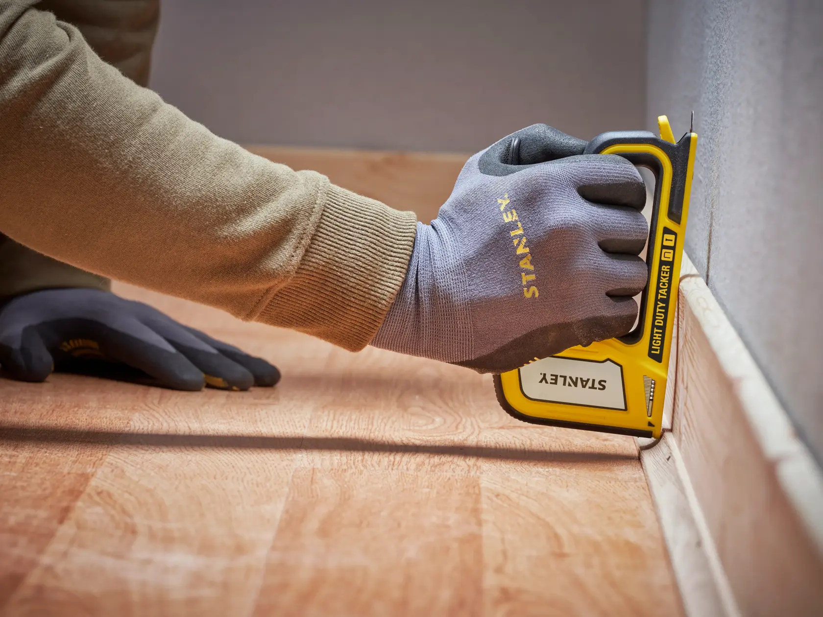 Stanley STHT70440 light duty tacker en uso sobre piso, ángulo cercano, persona con guantes Stanley.