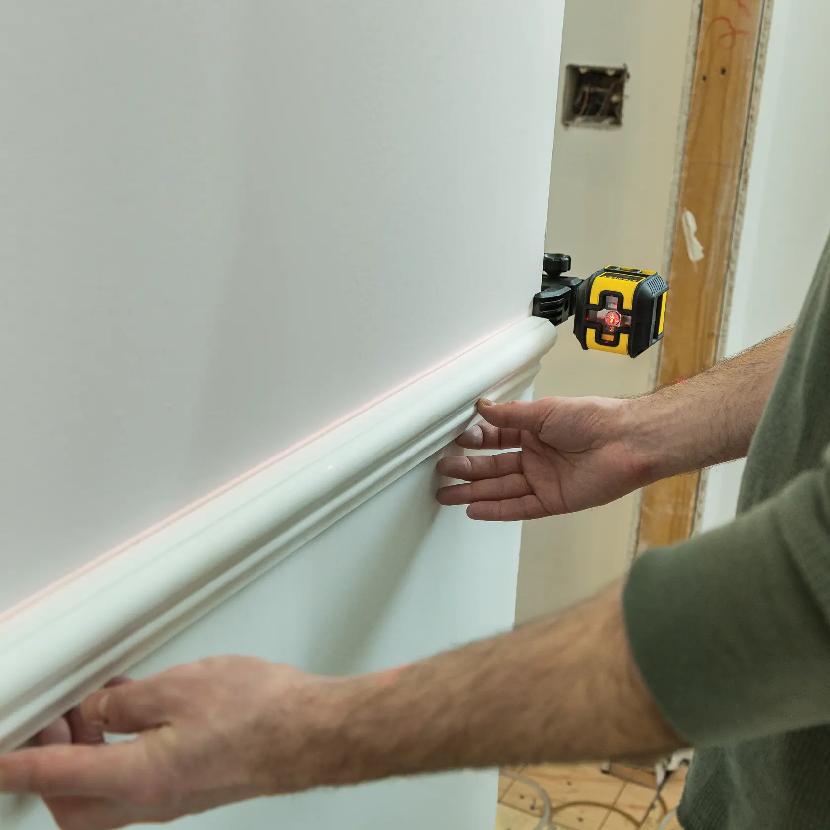 STANLEY STHT77498 nivel láser utilizado para alinear moldura blanca en pared interior, fotografía de primer plano.