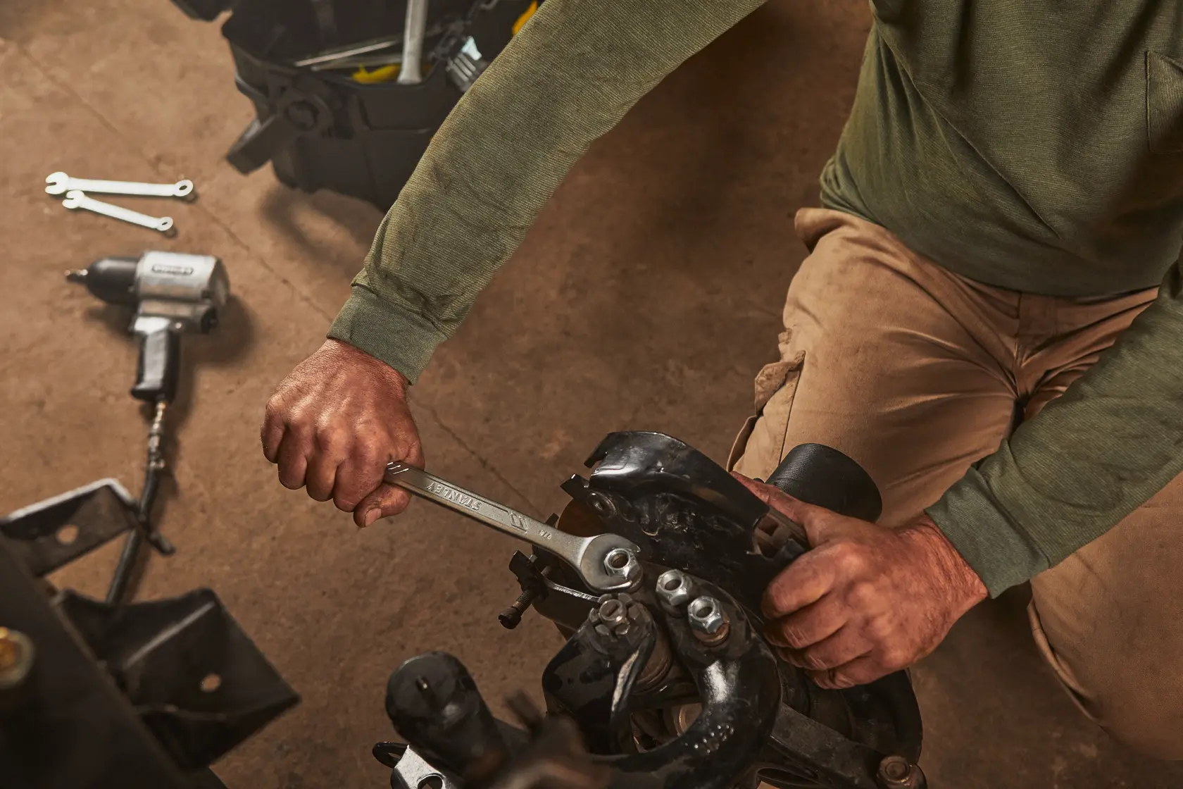 Llave STANLEY STMT72839 en uso ajustando un perno en maquinaria, con herramientas mecánicas visibles en el taller.