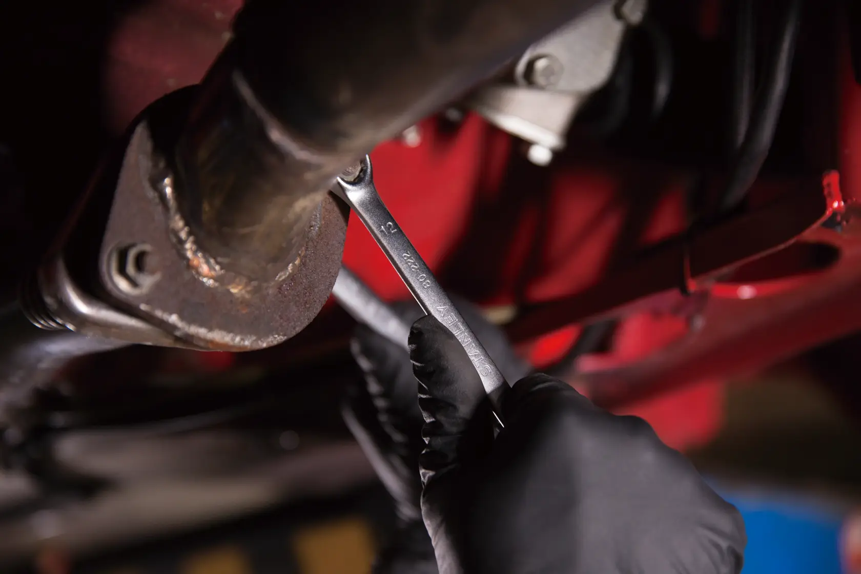 Llave STANLEY STMT80222 utilizada en una tubería por una mano enguantada en contexto automotriz.