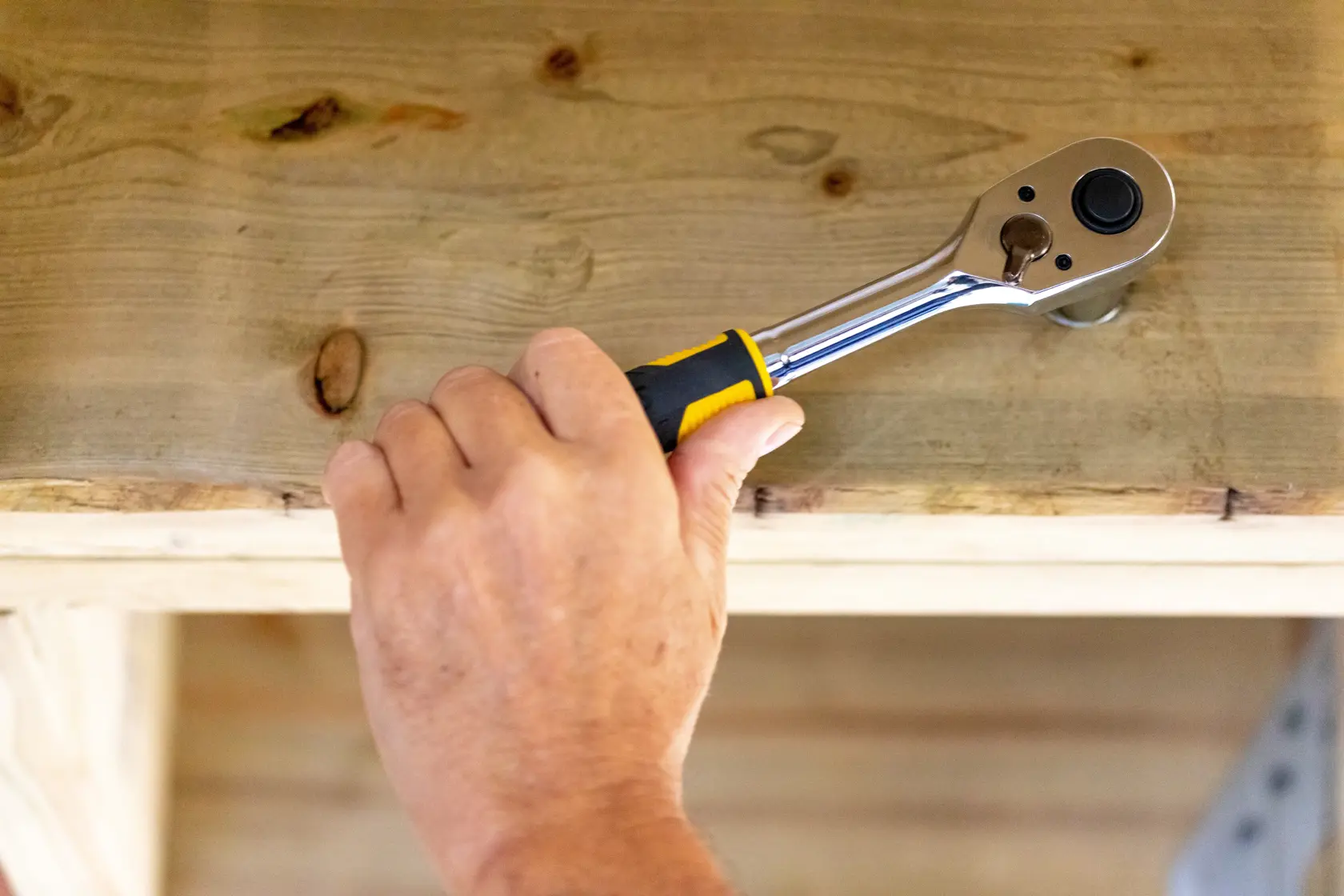Herramienta de carraca STANLEY STMT82665-0 usada en madera, primer plano de una mano sujetando la herramienta.