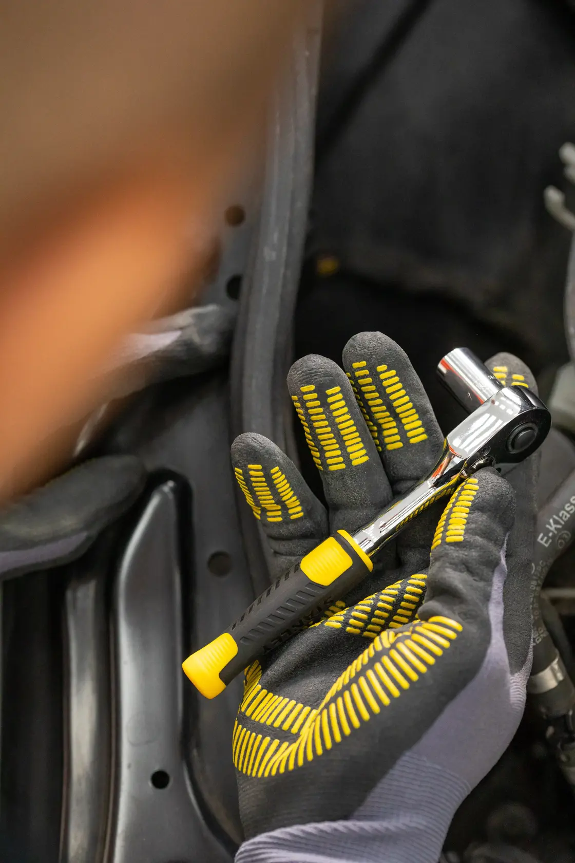 Llave de carraca STANLEY STMT82829-LA sostenida con guante, con mango negro y amarillo, primer plano.
