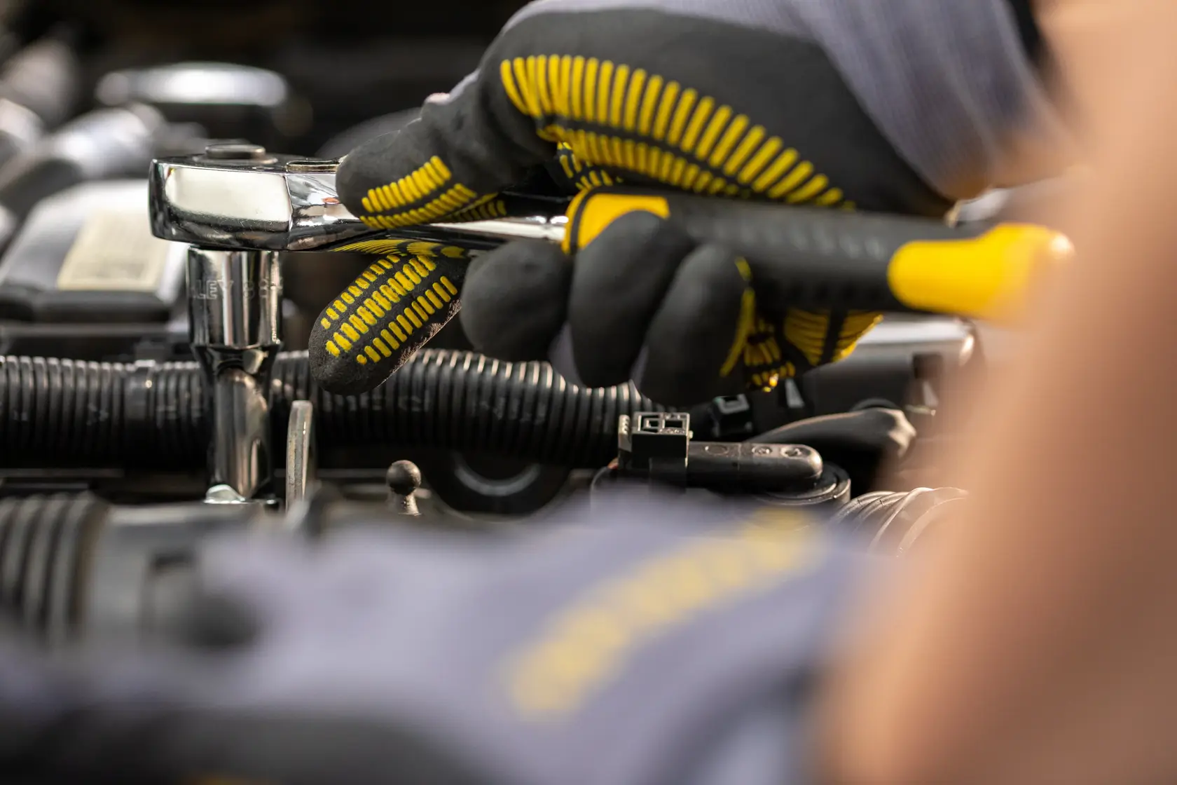 Llave de carraca STANLEY STMT82830-LA usada por una mano enguantada para reparación automotriz, primer plano.