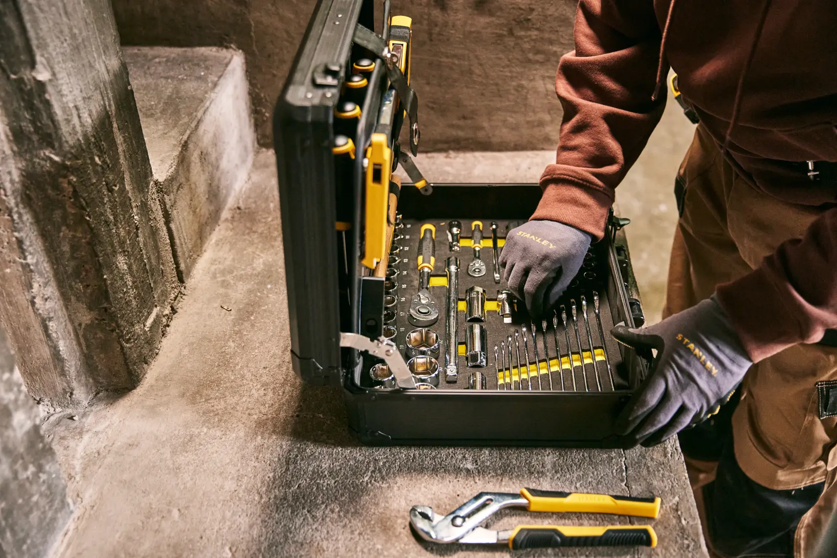 STANLEY STMT98109-LA juego de herramientas en caja negra, varias herramientas, trabajador usándolo, fotografía en superficie de concreto.