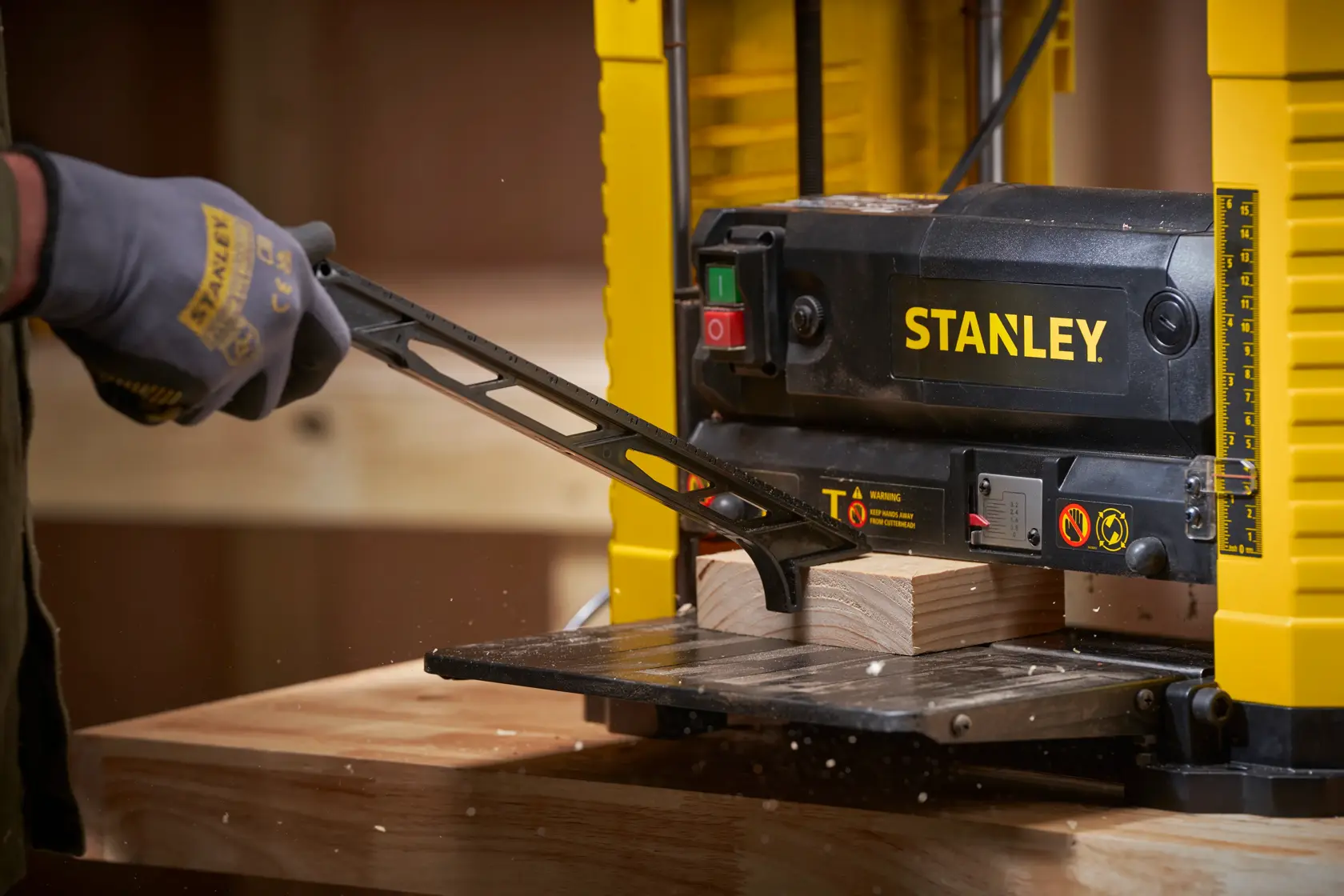 Fotografía de la cepilladora STANLEY STP18-B2 en uso, alisando una tabla de madera en un taller desde arriba.
