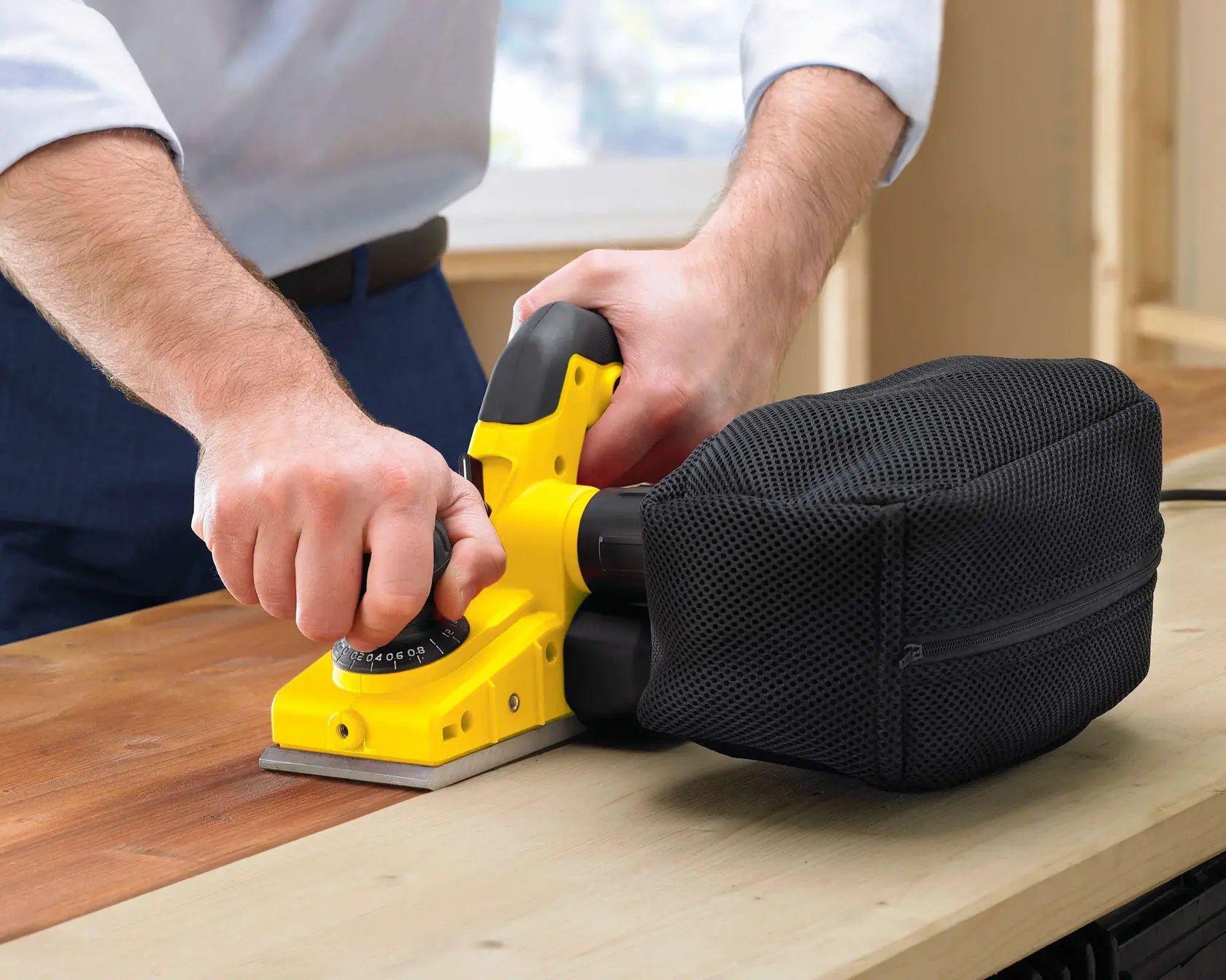 Fotografía del cepillo manual STANLEY STPP7502-B2 con bolsa recogepolvo negra lijando una superficie de madera, primer plano en uso.