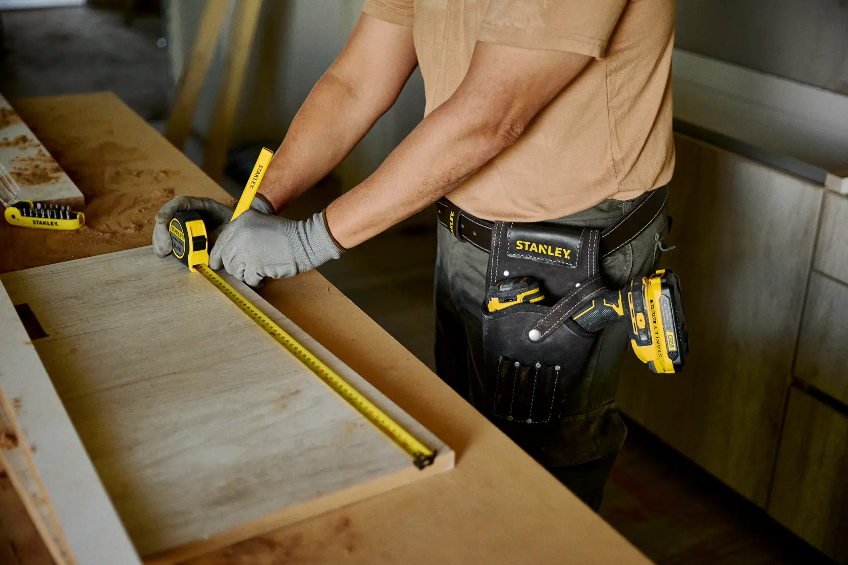 Fotografía del cinturón de herramientas STANLEY STST1-80118 usado por trabajador midiendo madera con cinta métrica en taller.