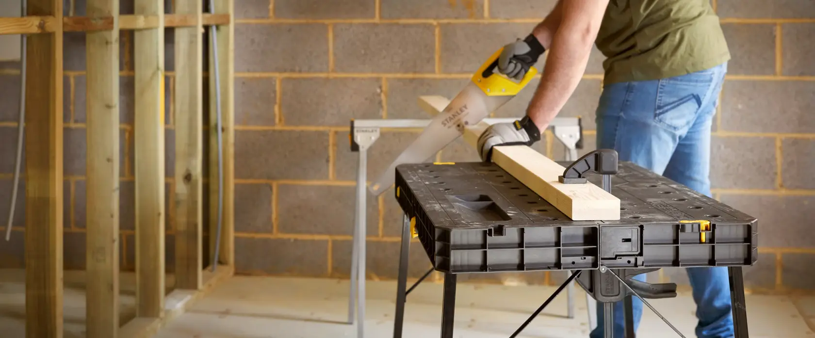 STANLEY STST11552 banco de trabajo, mesa plegable negra sosteniendo tabla de madera en taller.