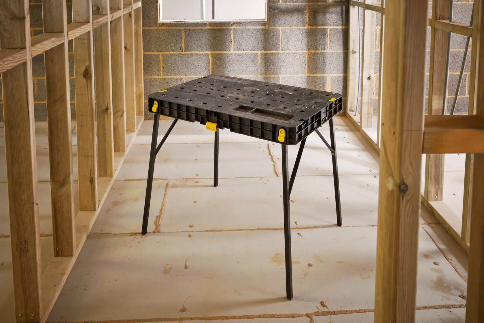 STANLEY STST11552 banco de trabajo plegable de plástico negro con patas de metal, visto en ángulo en obra en construcción.