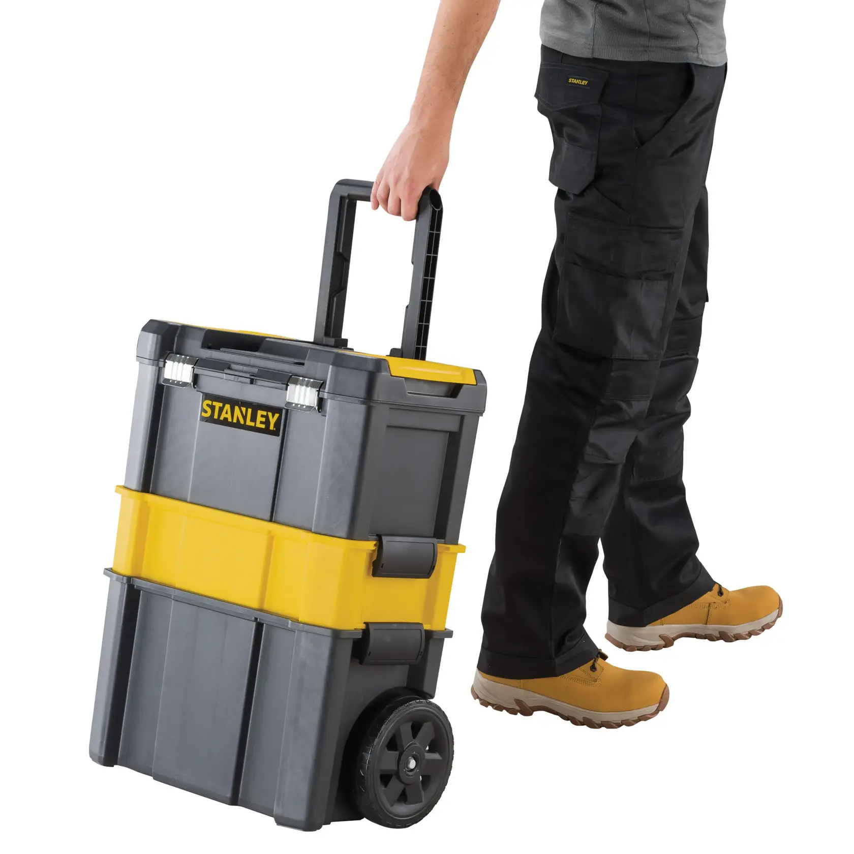 Caja de herramientas Stanley con ruedas, gris y amarilla, vista frontal, tirada por persona con pantalones y botas