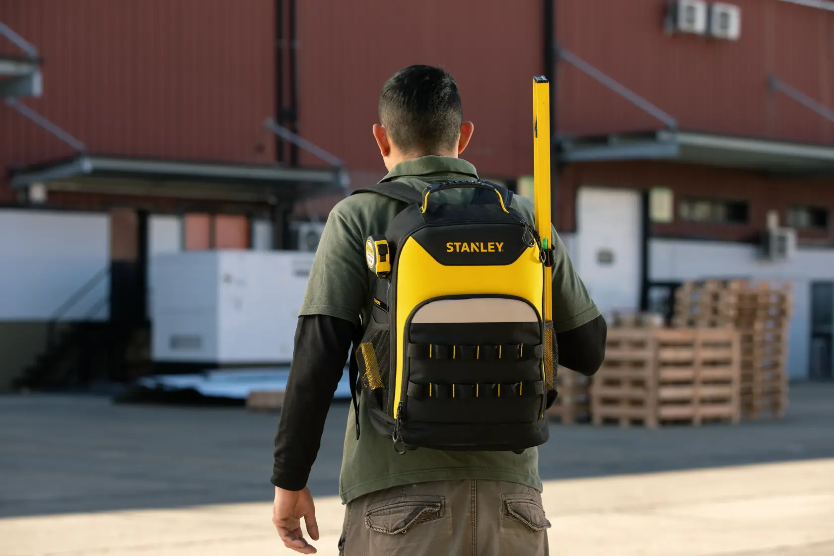Foto de la mochila STANLEY, SKU STST515155LA, negra y amarilla, usada al aire libre con herramientas en los bolsillos.