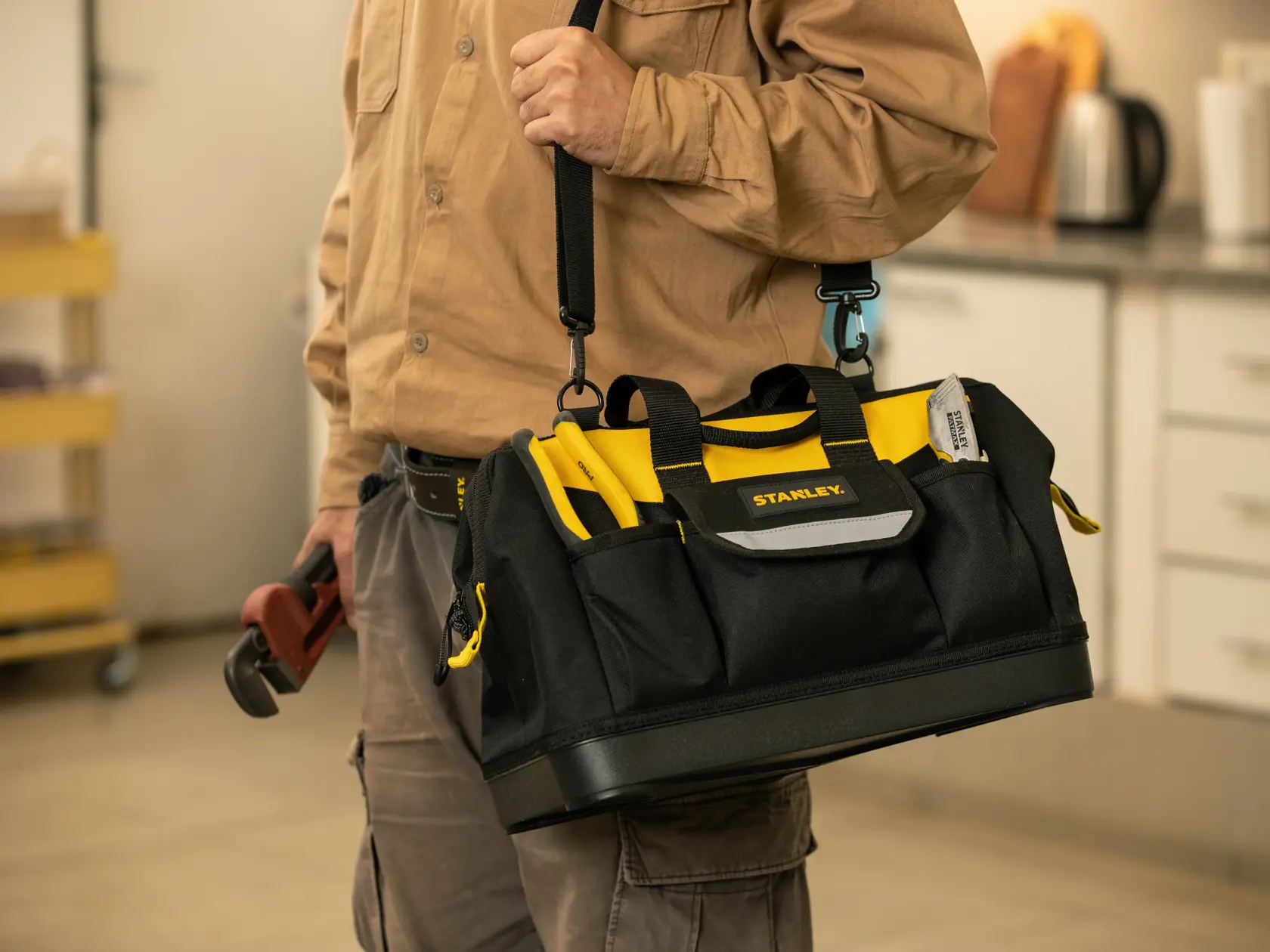Foto de la bolsa para herramientas STANLEY STST516126LA con asas amarillas, llevada en un taller.