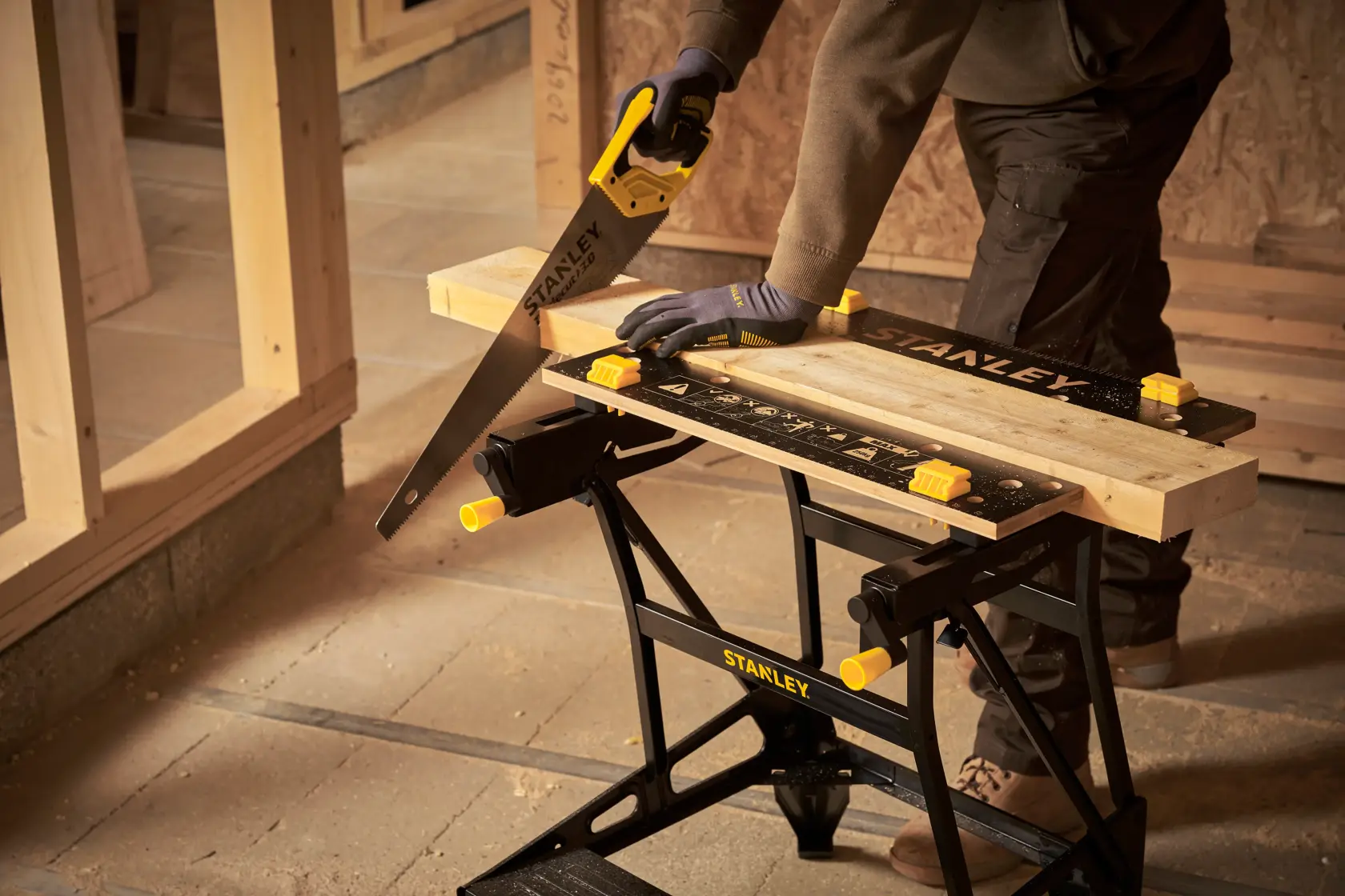 Banco de trabajo portátil STANLEY STST83400-1 con madera sujeta, serrucho cortando madera, taller.