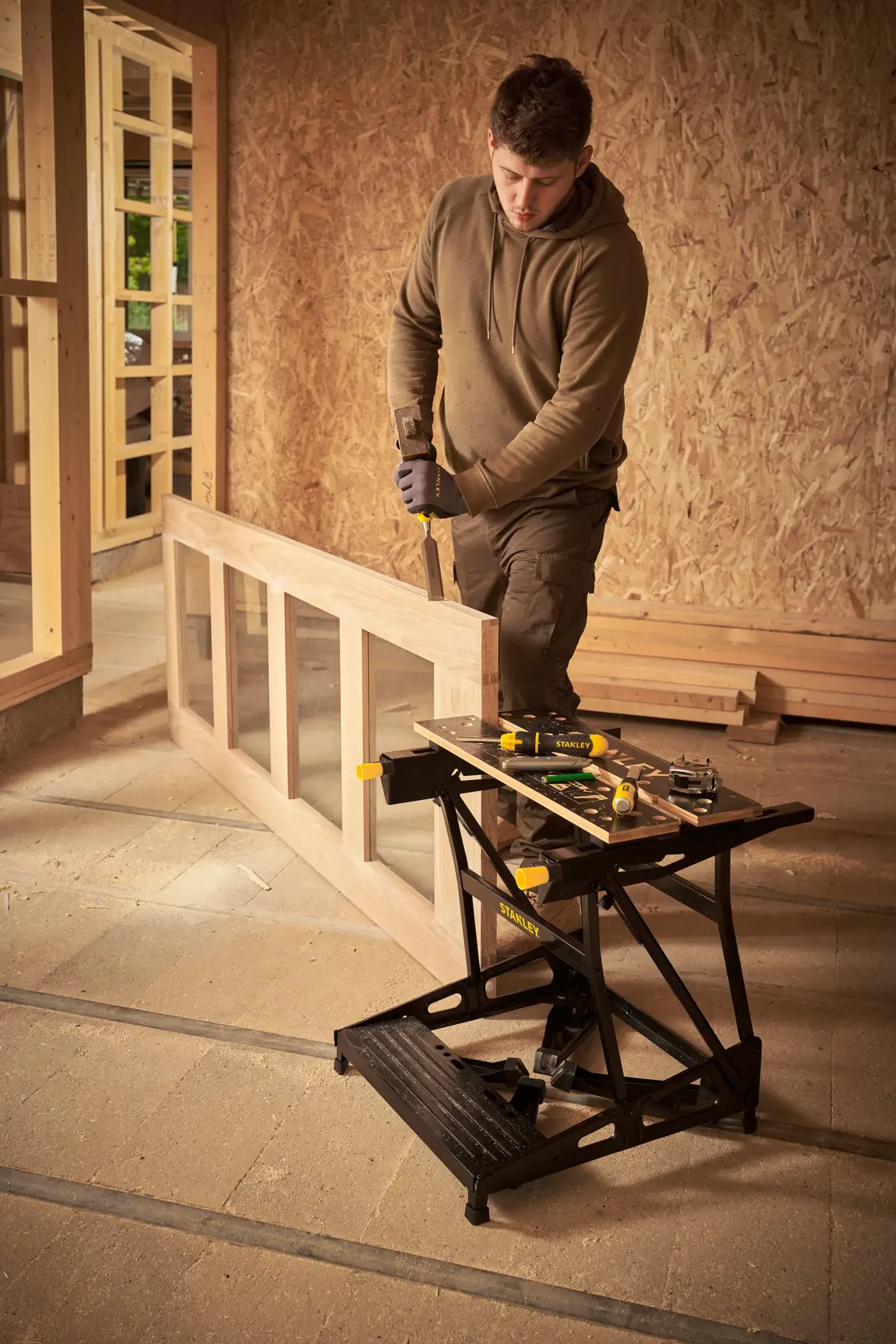 STANLEY STST83400-1 banco de trabajo plegable con herramientas, mostrado en uso en un taller de carpintería.