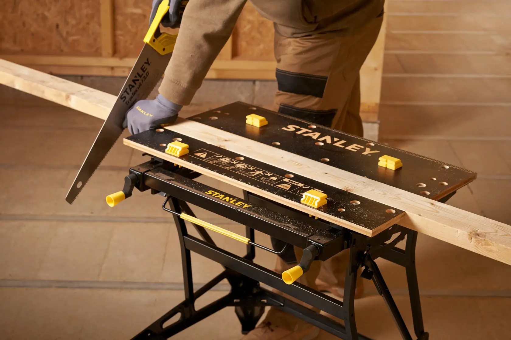 Stanley STST83800-1 banco de trabajo con tabla de madera, sierra manual y persona serrando en taller. Producto fotografía.