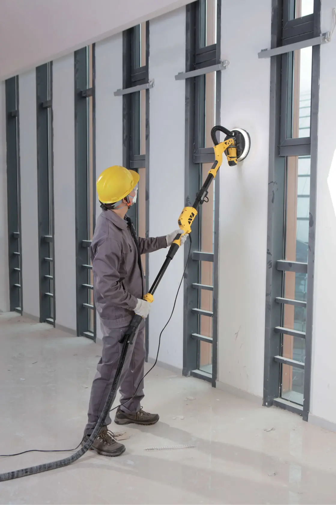 Stanley SW75-BR lijadora de paneles de yeso utilizada por trabajador con casco amarillo, lijando pared interior.